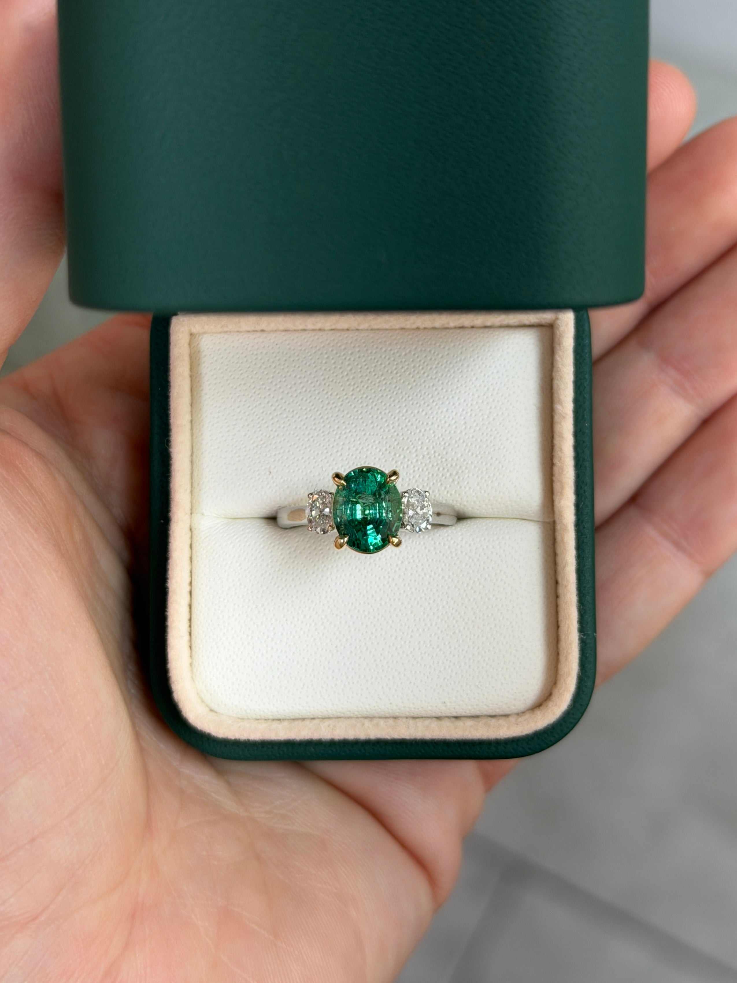 Vibrant oval emerald engagement ring with oval lab diamonds in platinum and 14K gold setting in green jewelry box