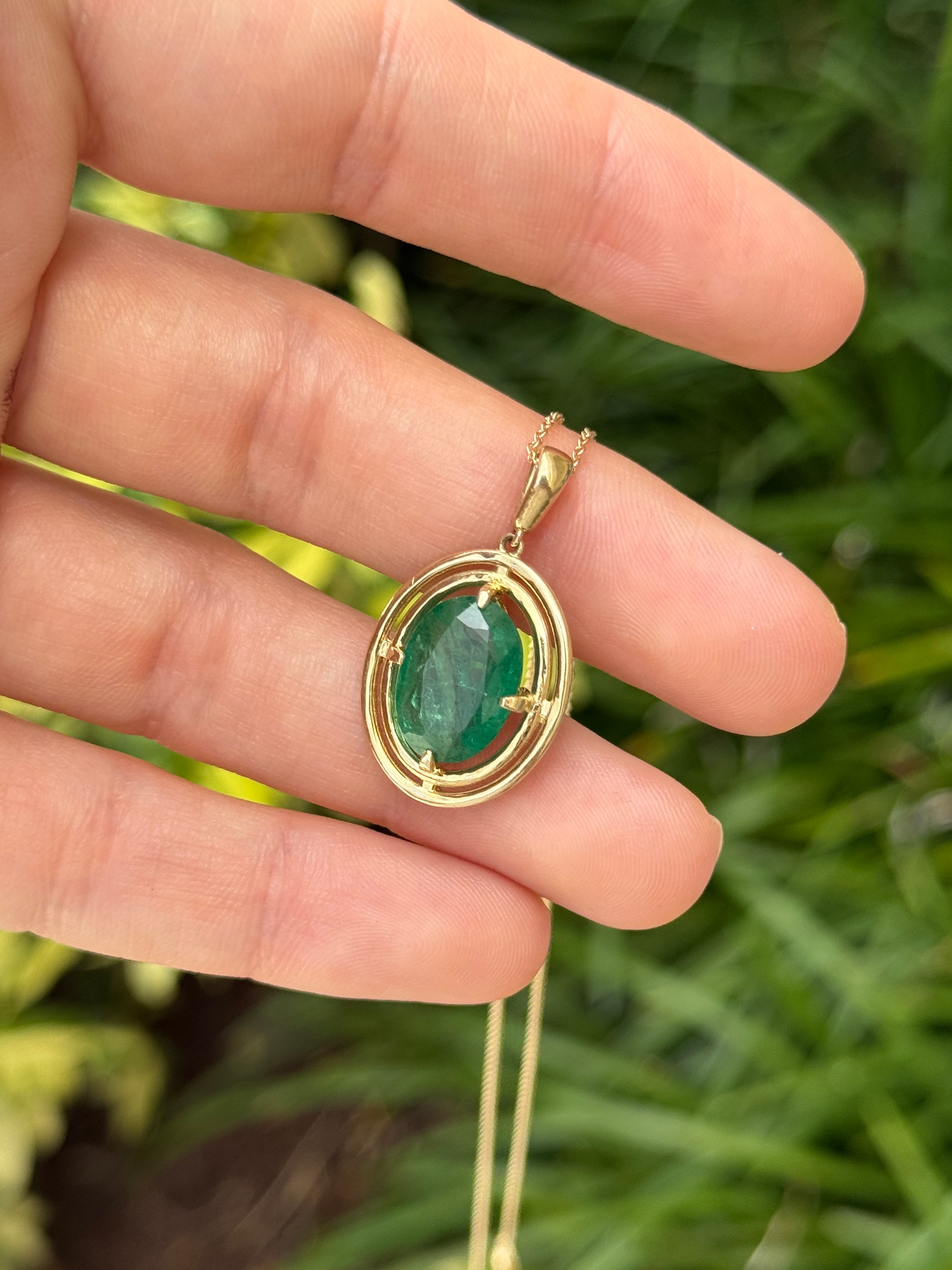 Ciondolo solitario con smeraldo ovale e doppia cornice a corona in oro giallo 14 carati, caratterizzato da una montatura a quattro griffe sospesa.
