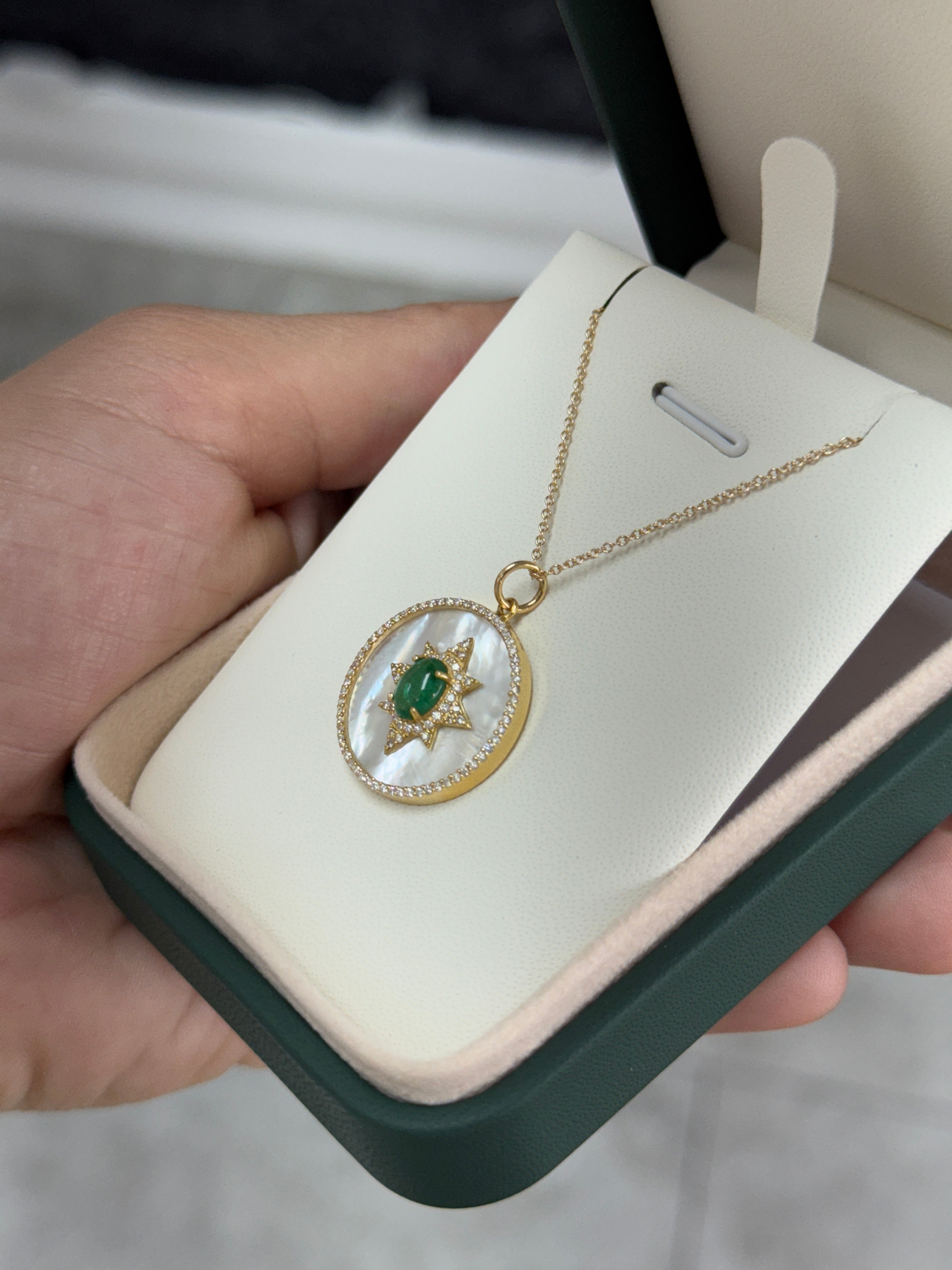 14K gold starburst medallion with emerald cabochon, mother of pearl, and diamond halo, featuring a detailed jewelry design.