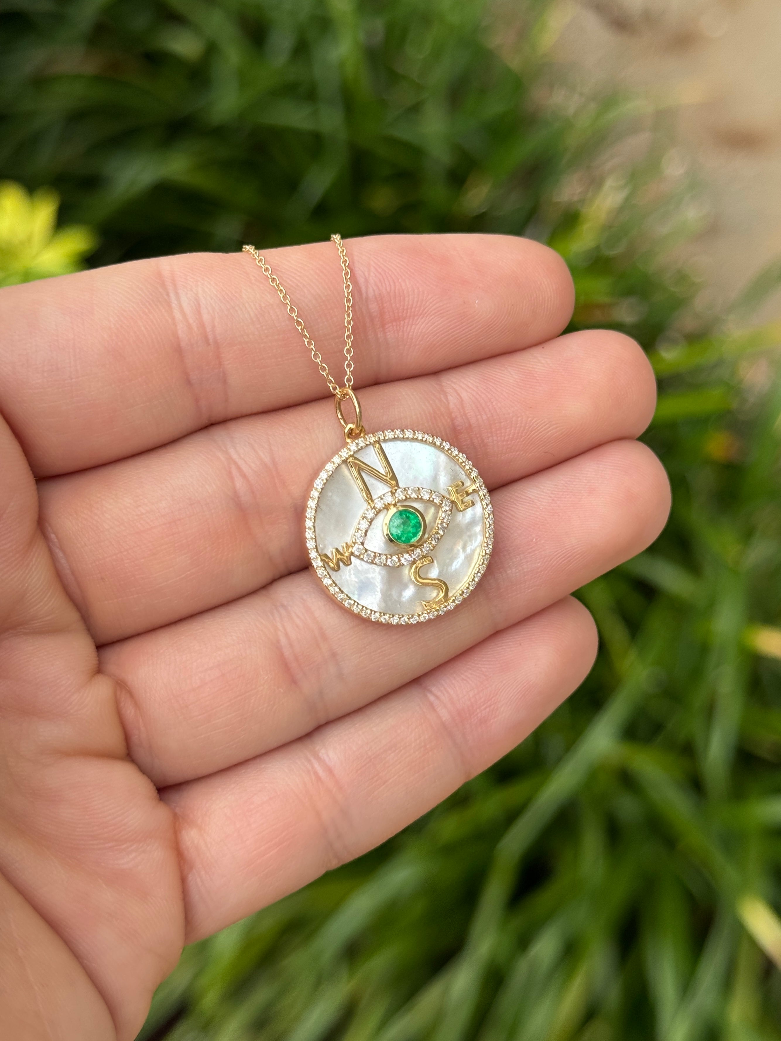 14K gold emerald and diamond compass evil eye pendant necklace with mother of pearl, featuring a round emerald and intricate design.