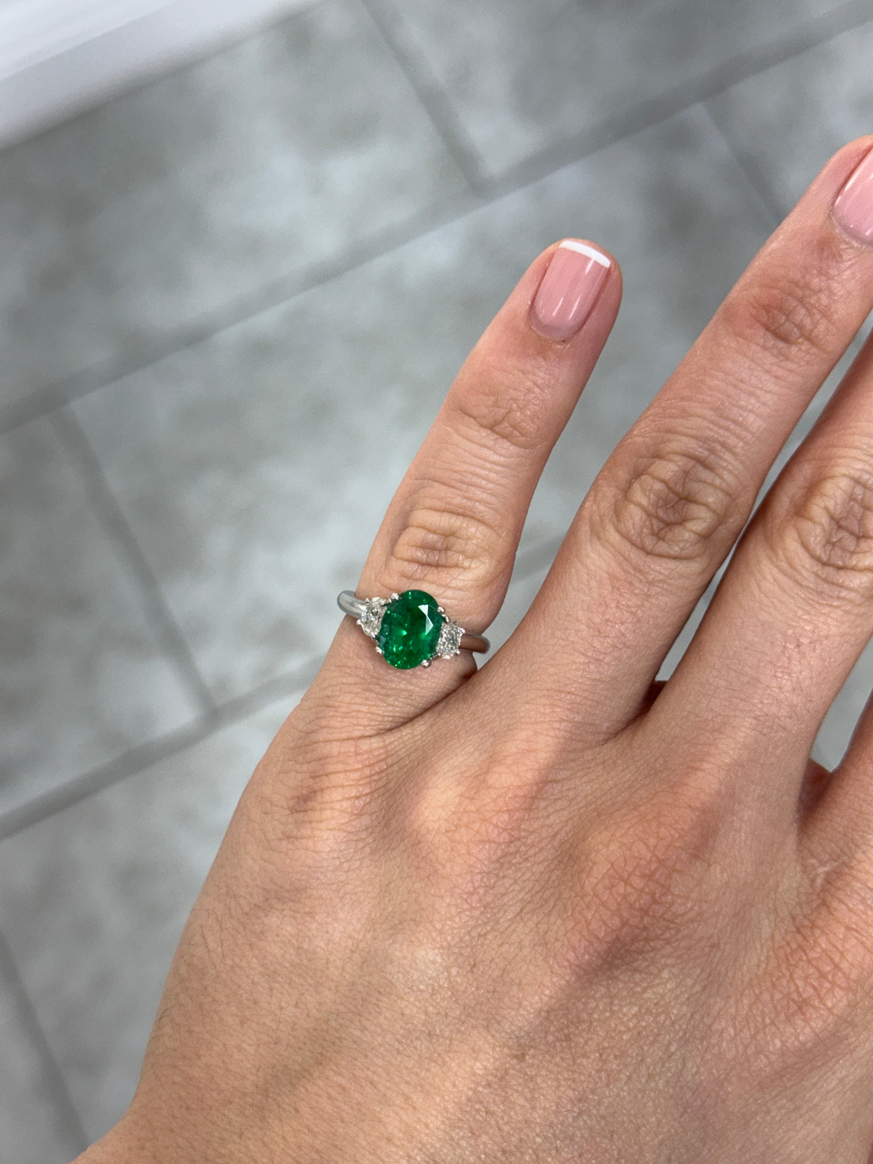 Vivid green oval emerald and oval diamond three-stone platinum ring by JR Colombian Emeralds, close-up of sparkling gemstones.