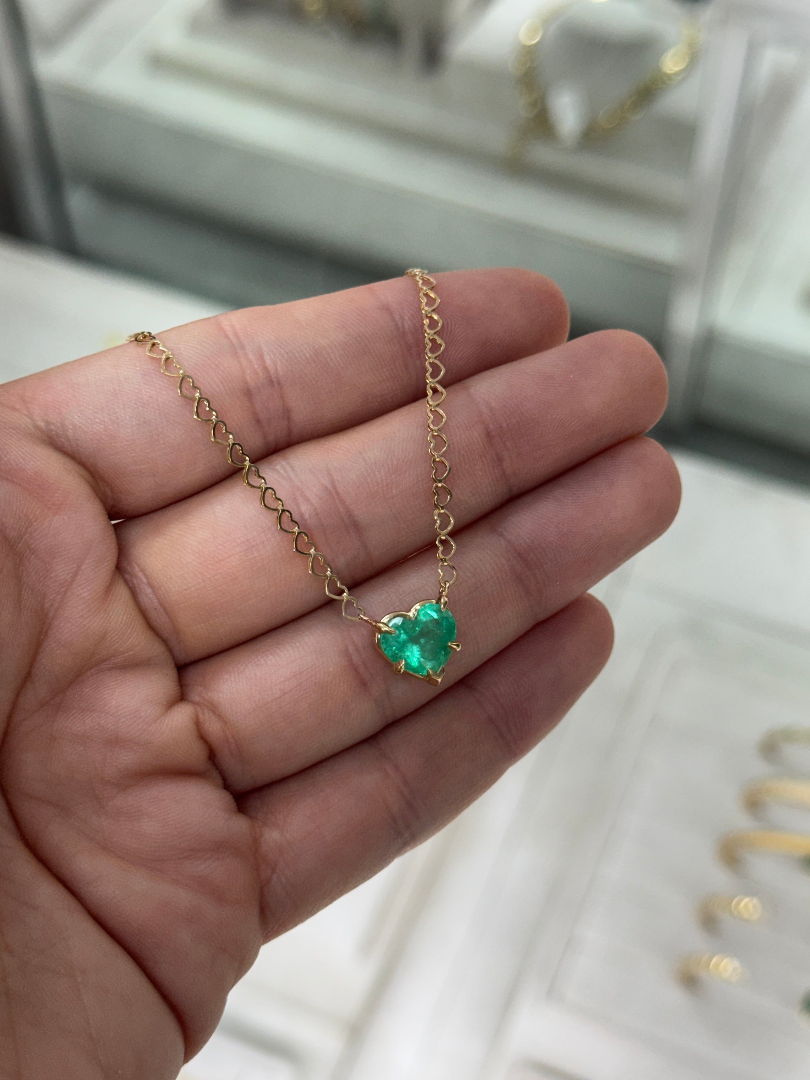 Natural Colombian emerald heart pendant on a 14K necklace with a solitaire station, showcased in a close-up image.