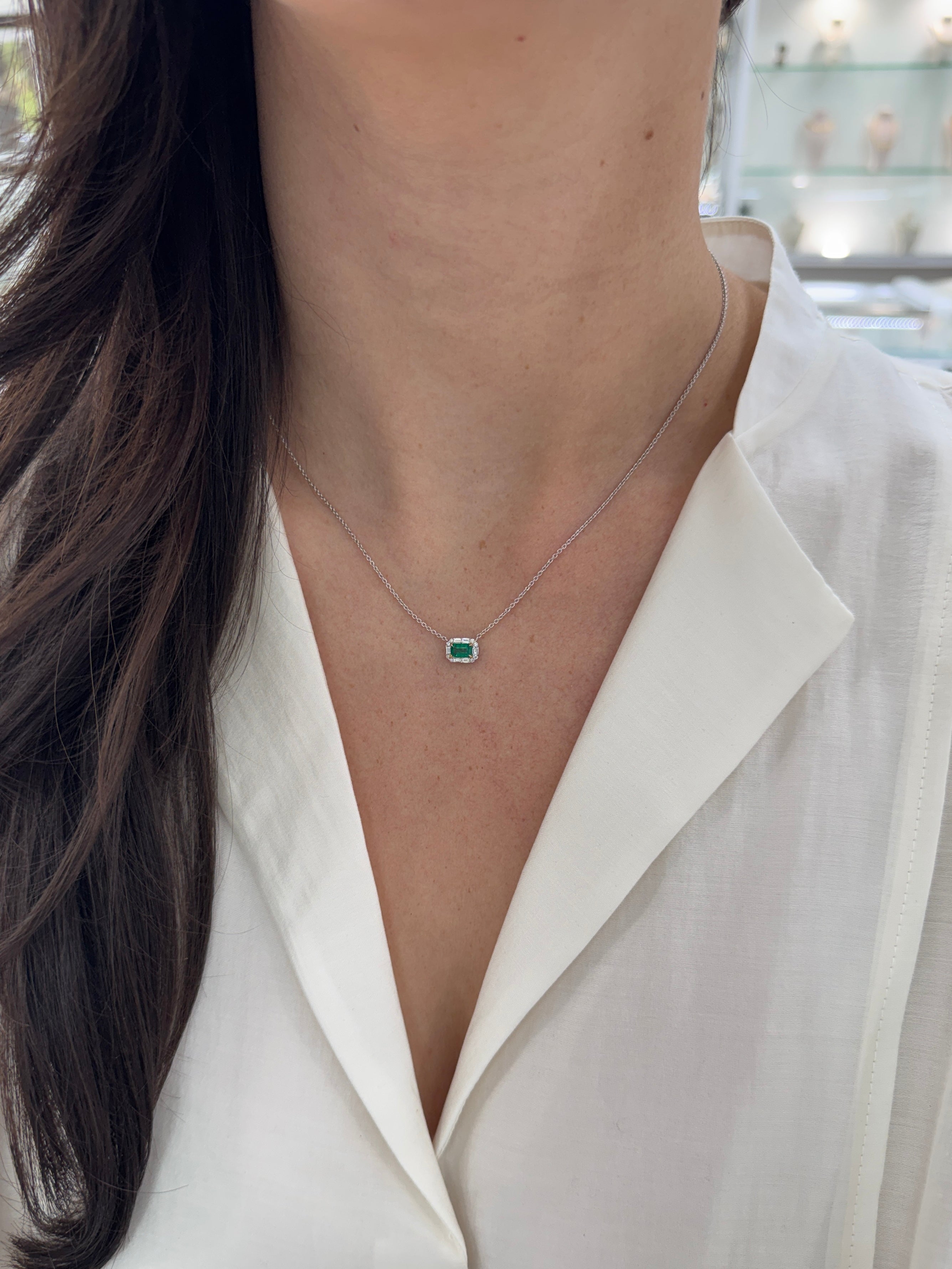 AAA+ natural emerald and baguette diamond halo necklace in 18K gold, featuring a green emerald centerpiece and east-west station design.