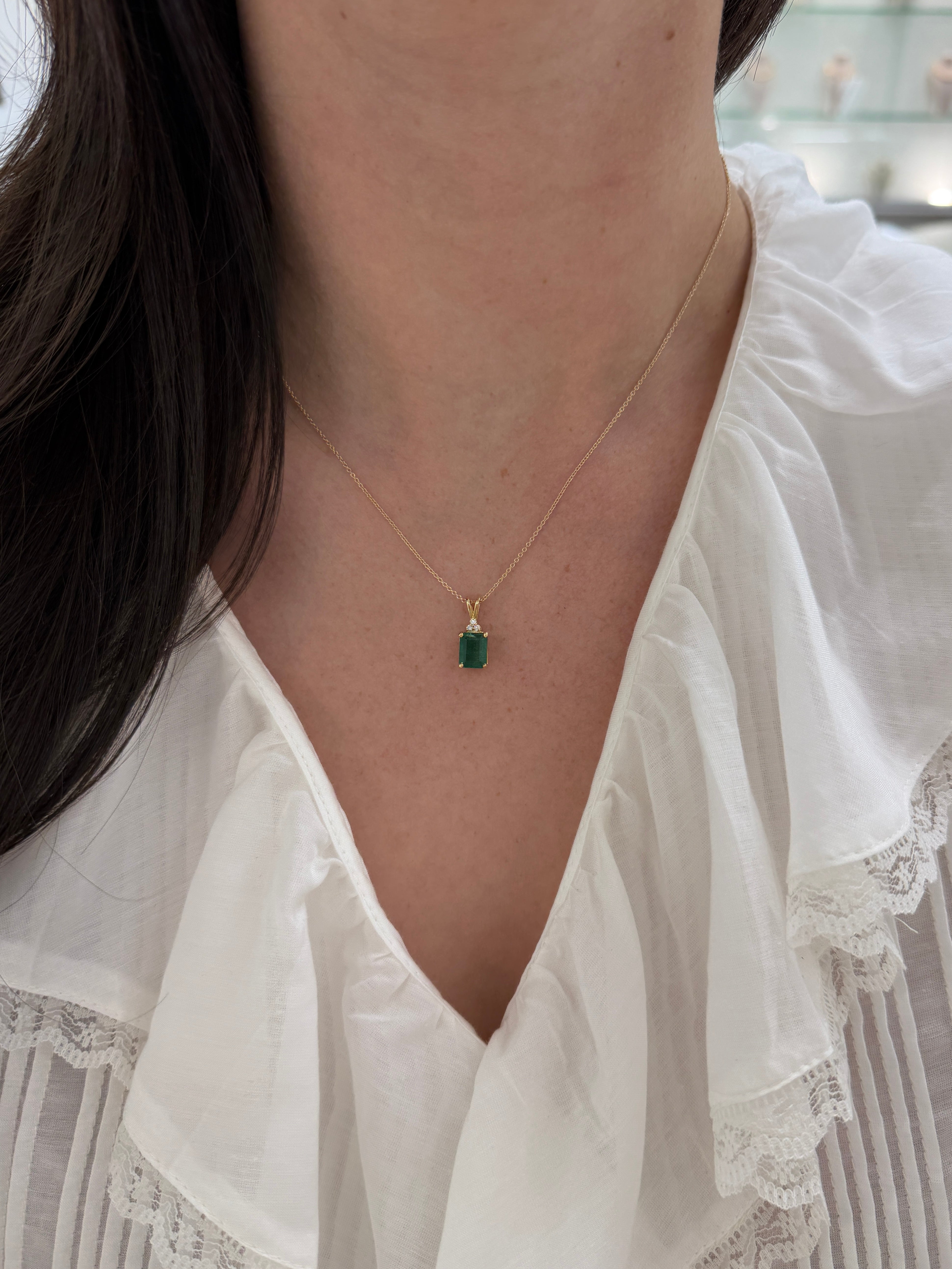 Emerald cut emerald pendant with trefoil diamond accents in 14K gold from JR Colombian Emeralds, showcasing a sparkling gemstone and detailed design.