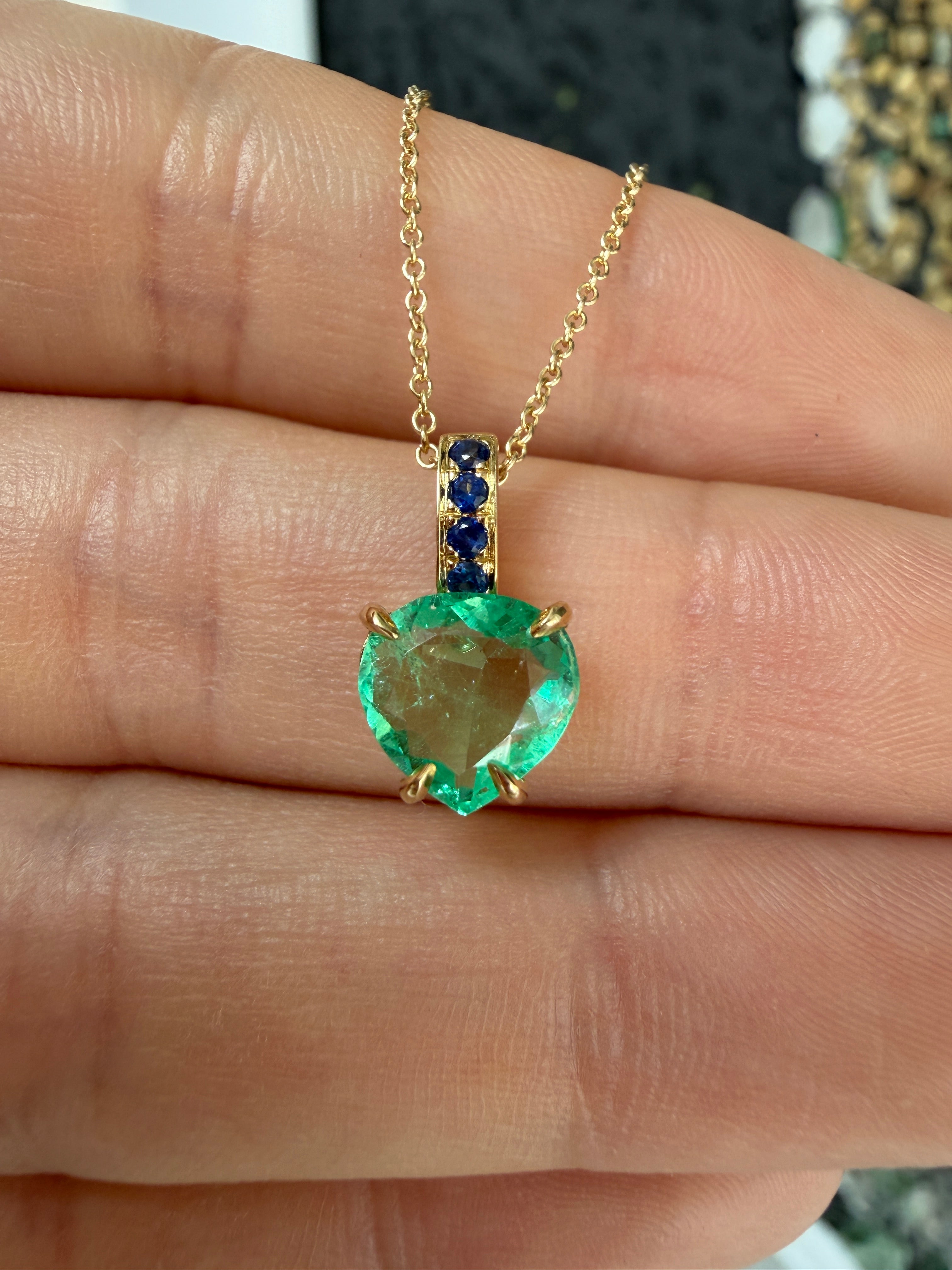 Colombian pear-shaped emerald pendant with blue sapphire bail in 14K gold, featuring a heart design by JR Colombian Emeralds.