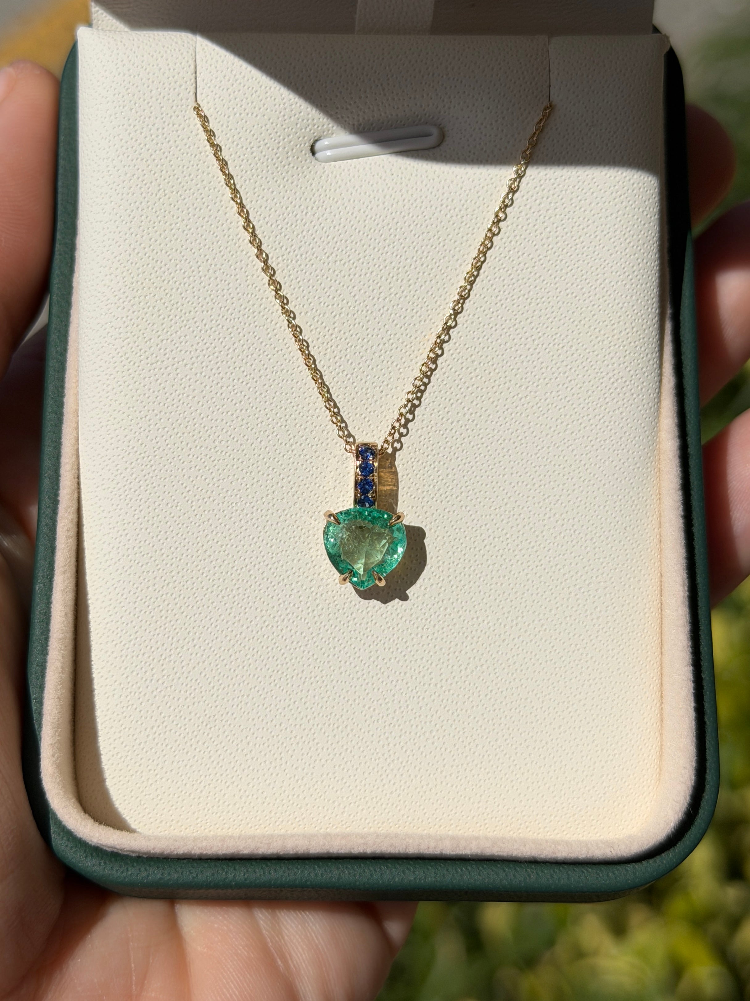 Colombian pear-shaped emerald pendant with blue sapphire bail in 14K gold, featuring a heart design by JR Colombian Emeralds.