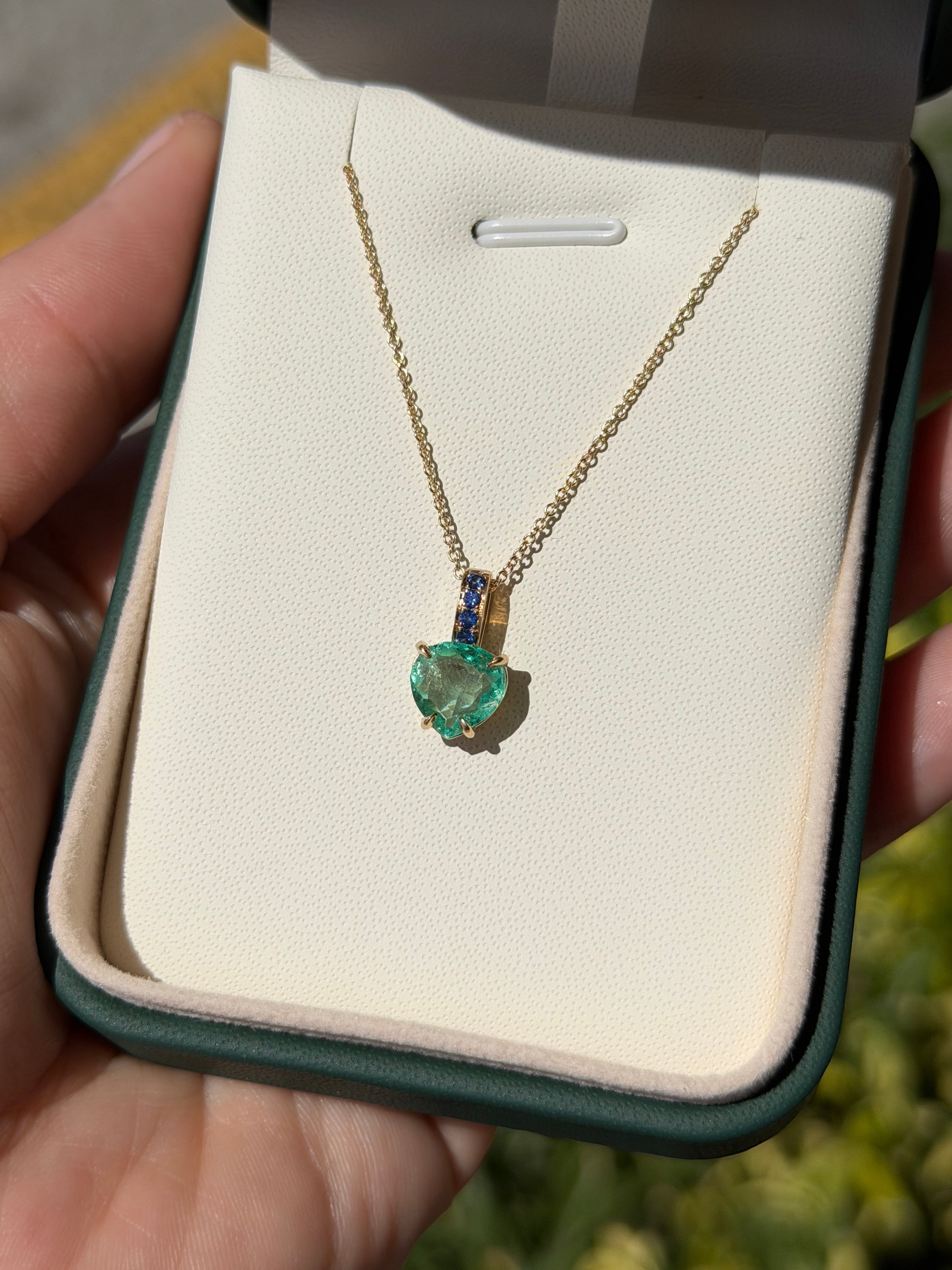 Colombian pear-shaped emerald pendant with blue sapphire bail in 14K gold, featuring a heart-shaped design by JR Colombian Emeralds.
