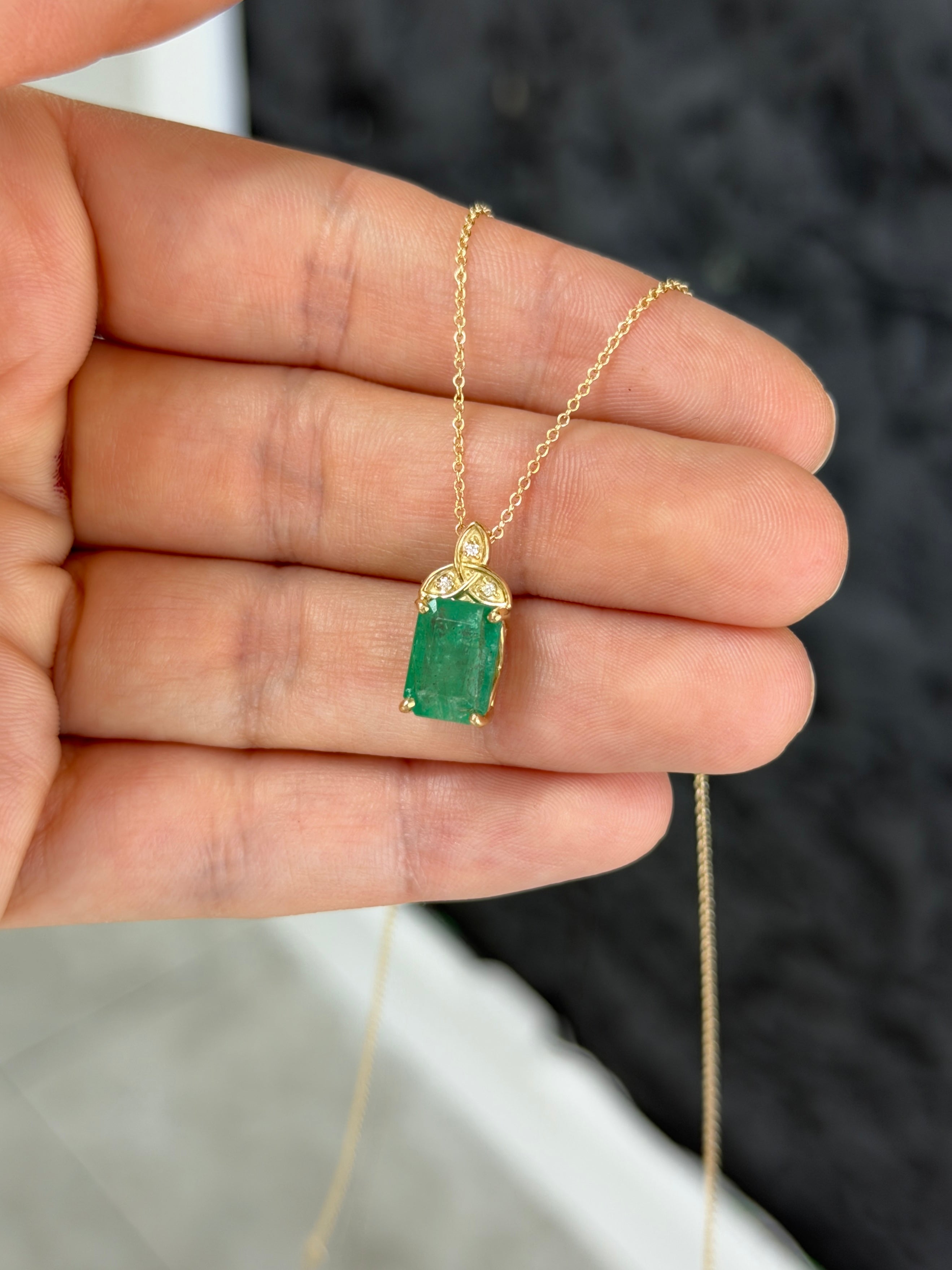 14K yellow gold Trinity knot emerald solitaire necklace with 2.12tcw from JR Colombian Emeralds, close-up of pendant on chain.