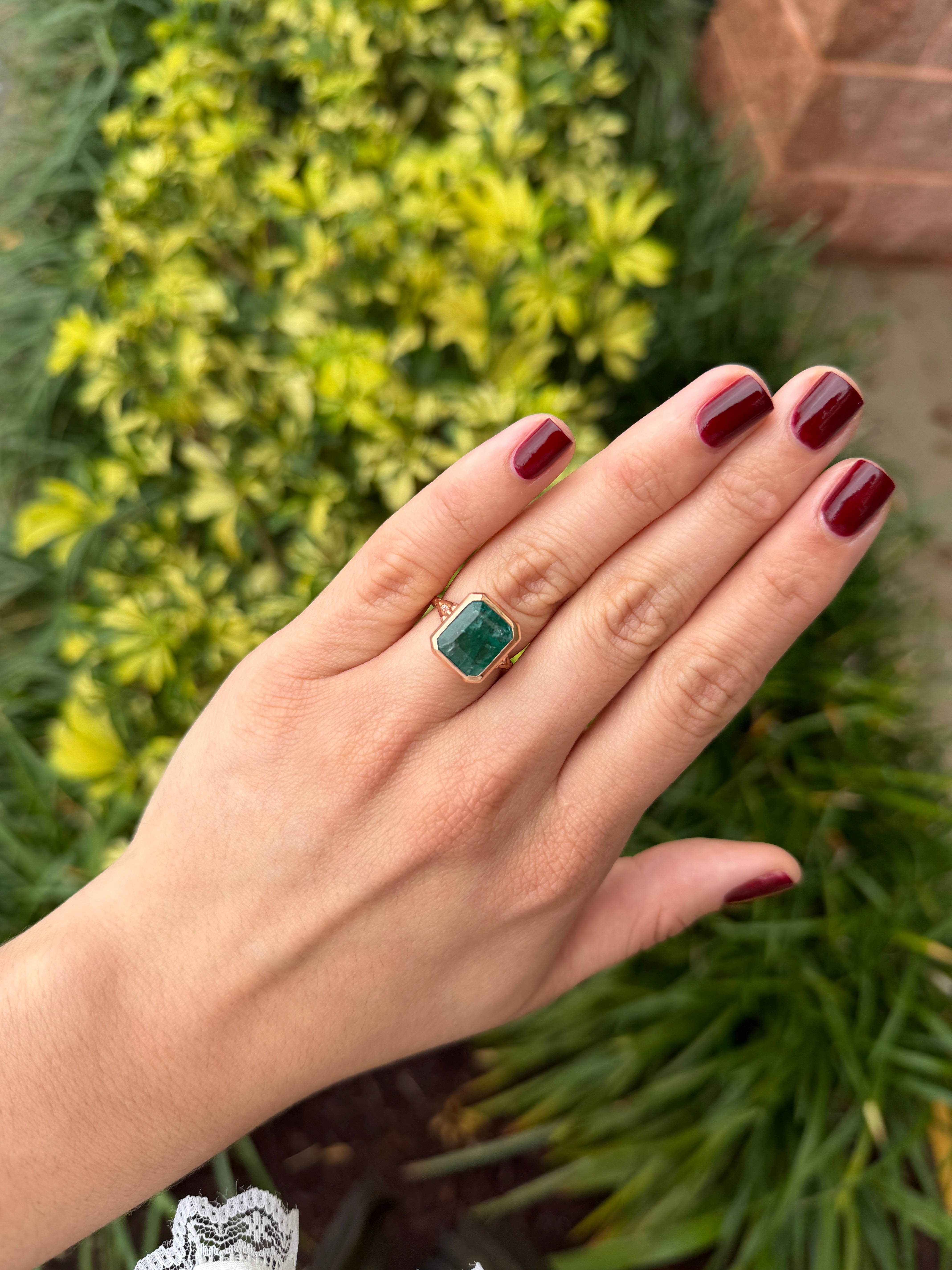 Vintage-inspired 14K rose gold emerald bezel ring with diamond shank and scroll basket detail, featuring 6.20tcw of gemstones.