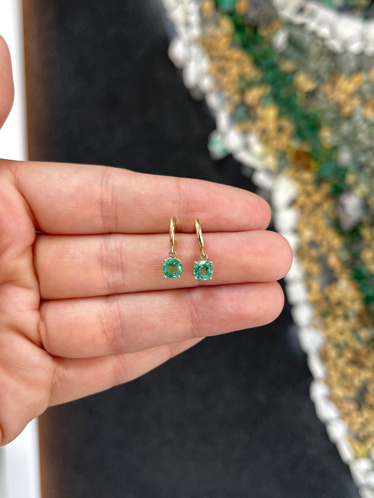 Medium dark green emerald round cut huggie hoop earrings in 14K gold with four prongs, featuring Colombian Emerald brand.