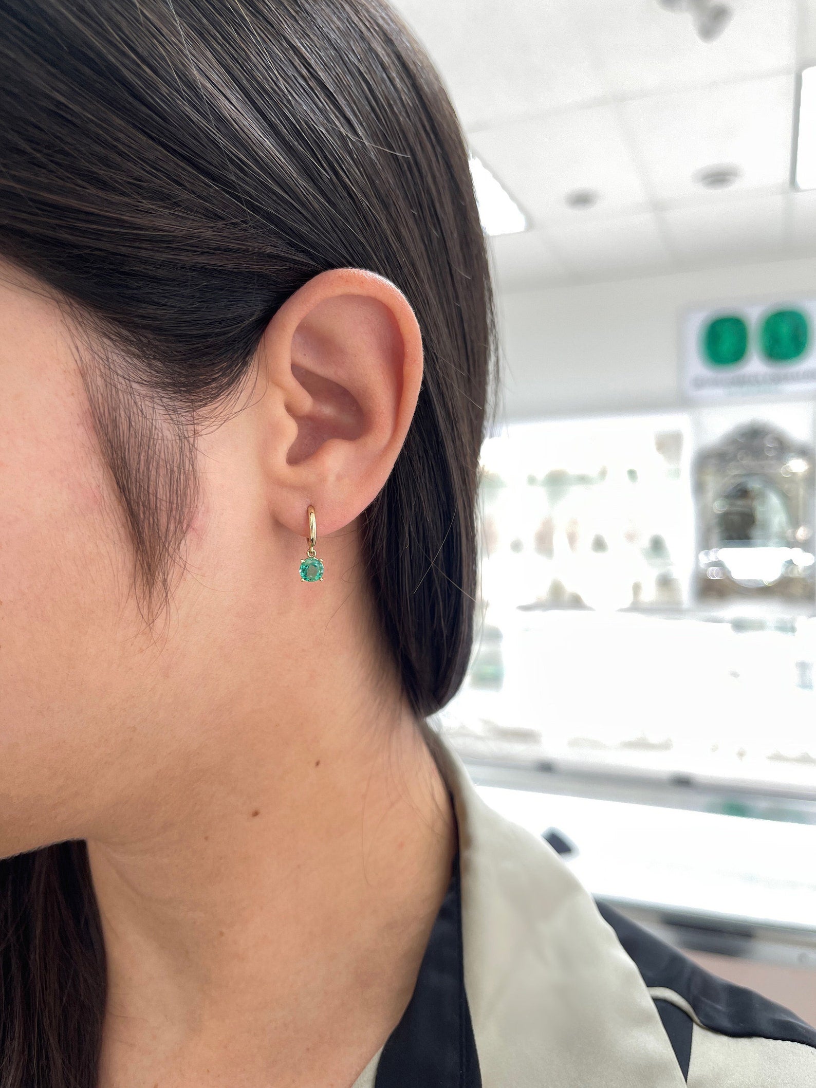 Medium dark green emerald round cut hoop earrings with four prongs in 14K gold, Colombian Emerald brand.