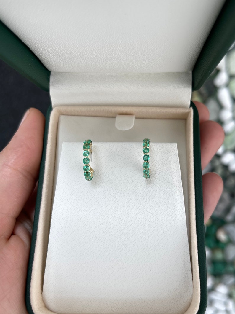Colombian Emerald 14K yellow gold hoop earrings with 1.50tcw round cut green emeralds, prong set in half hoop huggie style.