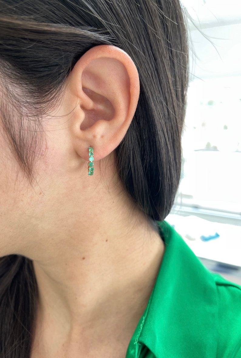Colombian Emerald 14K yellow gold half hoop huggie earrings with round cut green emeralds and prong settings.