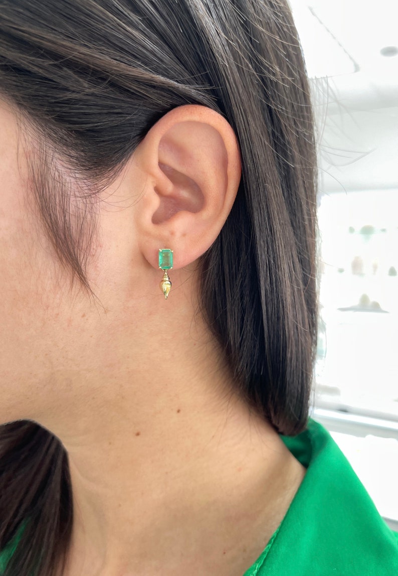 14K gold emerald and sea shell dangle earrings featuring 1.80tcw natural Colombian emeralds and sea shell accents.