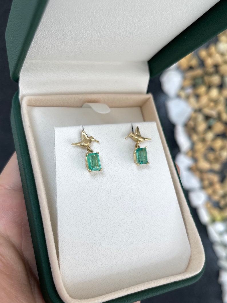 14K gold hummingbird dangle earrings with natural emeralds, featuring intricate bird designs and sparkling gemstones.