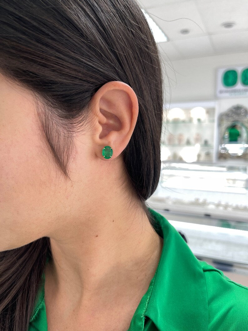 Colombian Emerald 4.85tcw 18K gold oval cut dark green stud earrings with four-prong claw setting.