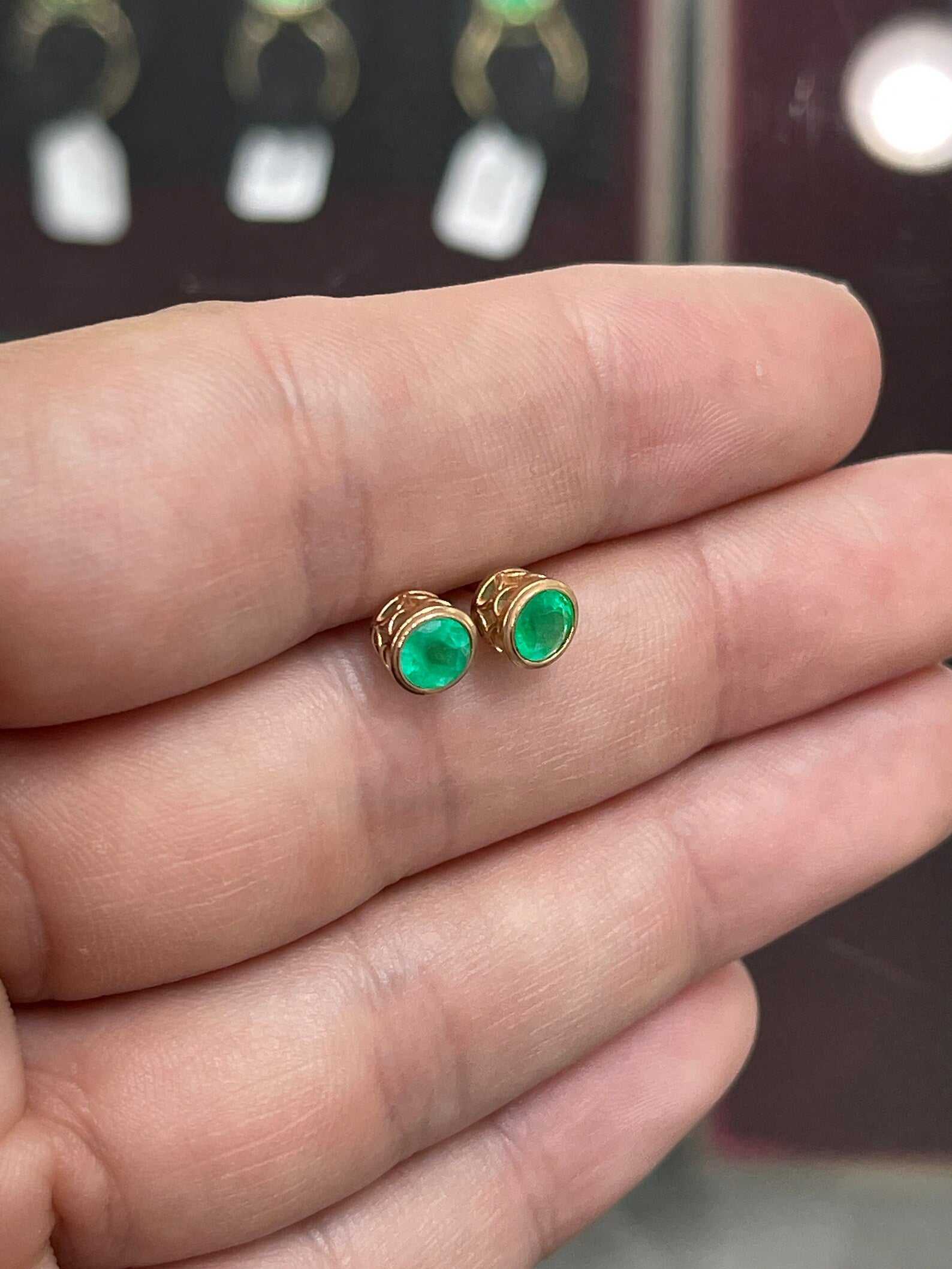 Rich green emerald round cut bezel set stud earrings in 14K yellow gold, featuring 1.40tcw Colombian emeralds.