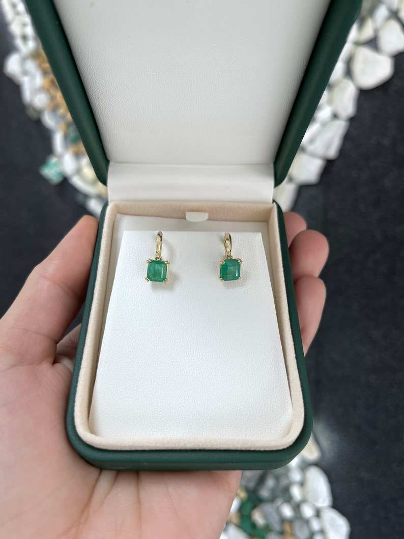 Colombian Emerald 2.80tcw natural Asscher cut knife-edge huggie dangle earrings in 14K yellow gold with emerald accents.