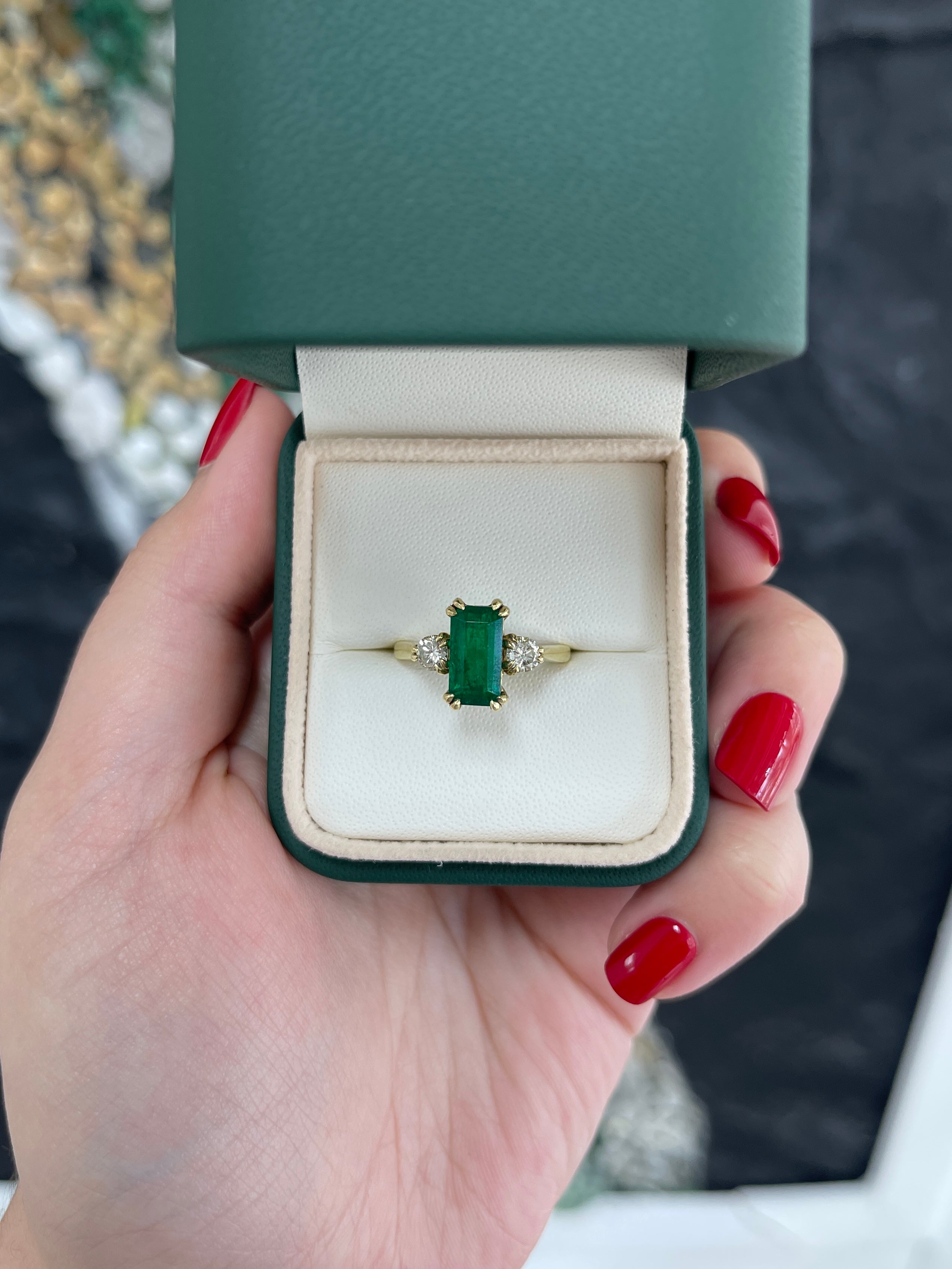 Colombian Emerald 18K three-stone engagement ring with deep green emerald cut and round diamonds, elegant and luxurious jewelry.
