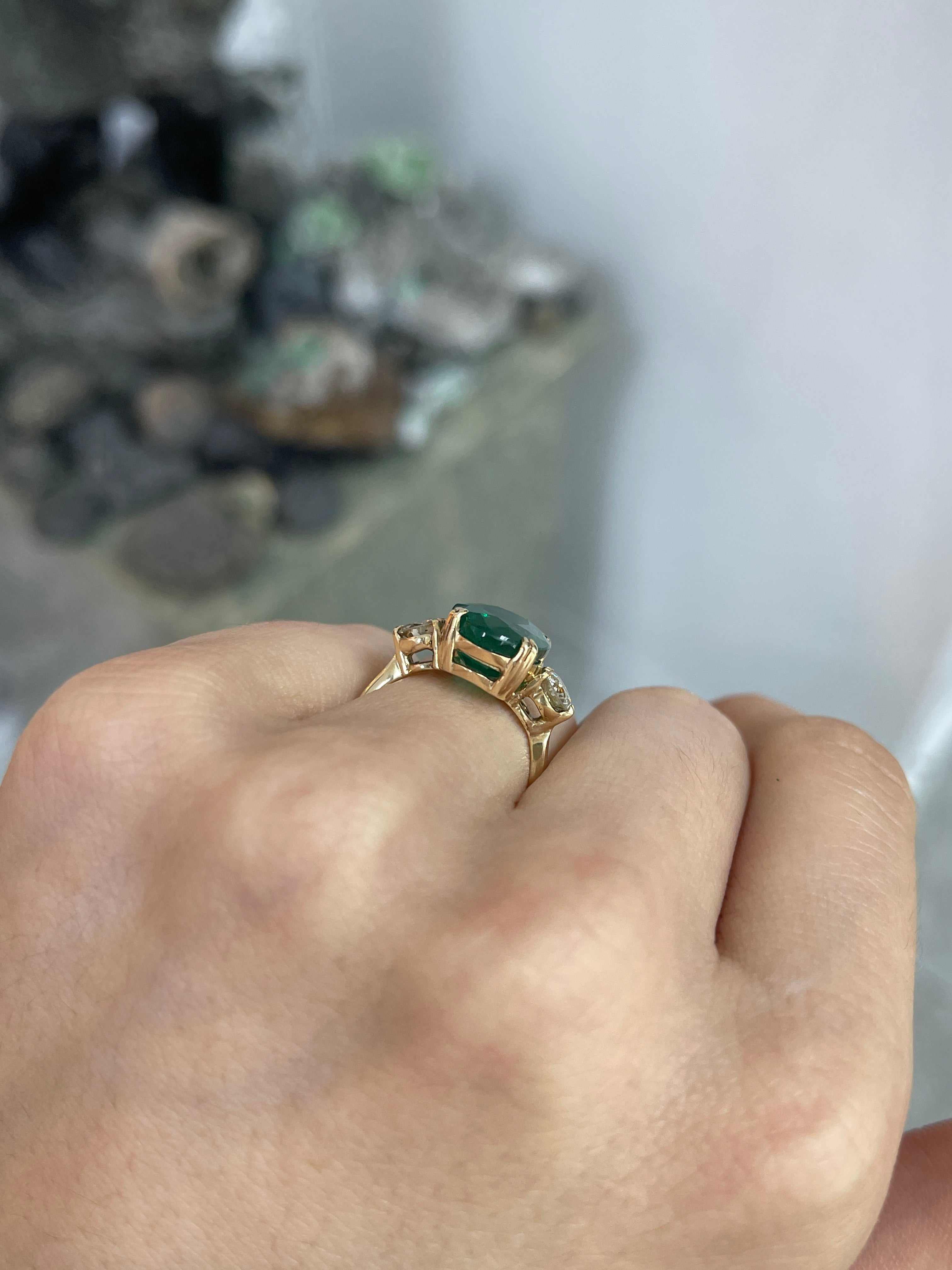 Dark green oval emerald and round diamonds in a 14K Colombian emerald engagement ring with double prong setting.