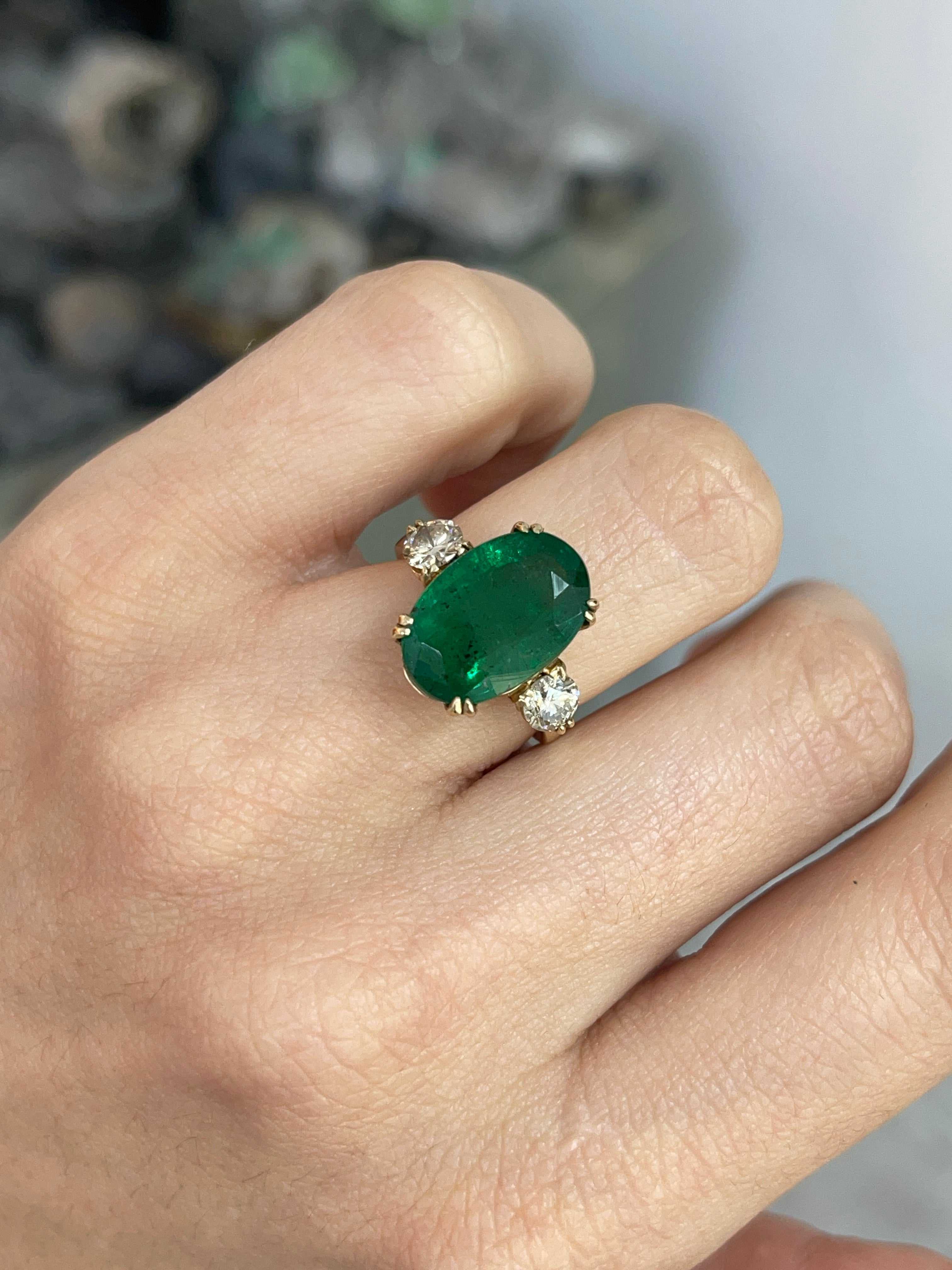 Dark green oval emerald and round diamonds in a 14K Colombian Emerald engagement ring with double prong setting.