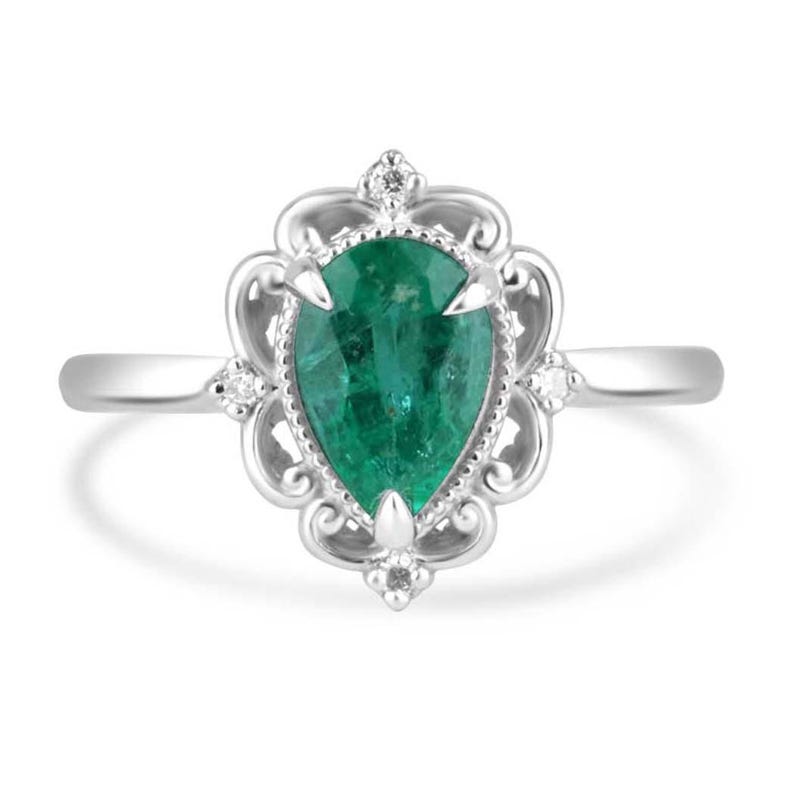 Platinum engagement ring with pear-shaped emerald and diamond accents, featuring intricate filigree crown scroll design.
