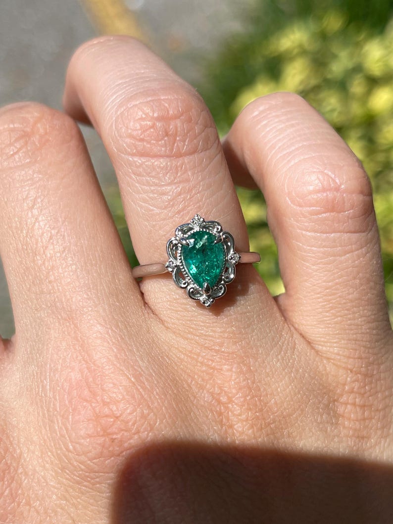 Platinum pear-shaped engagement ring with emerald and diamond accents, featuring intricate filigree scroll design by Colombian Emerald.