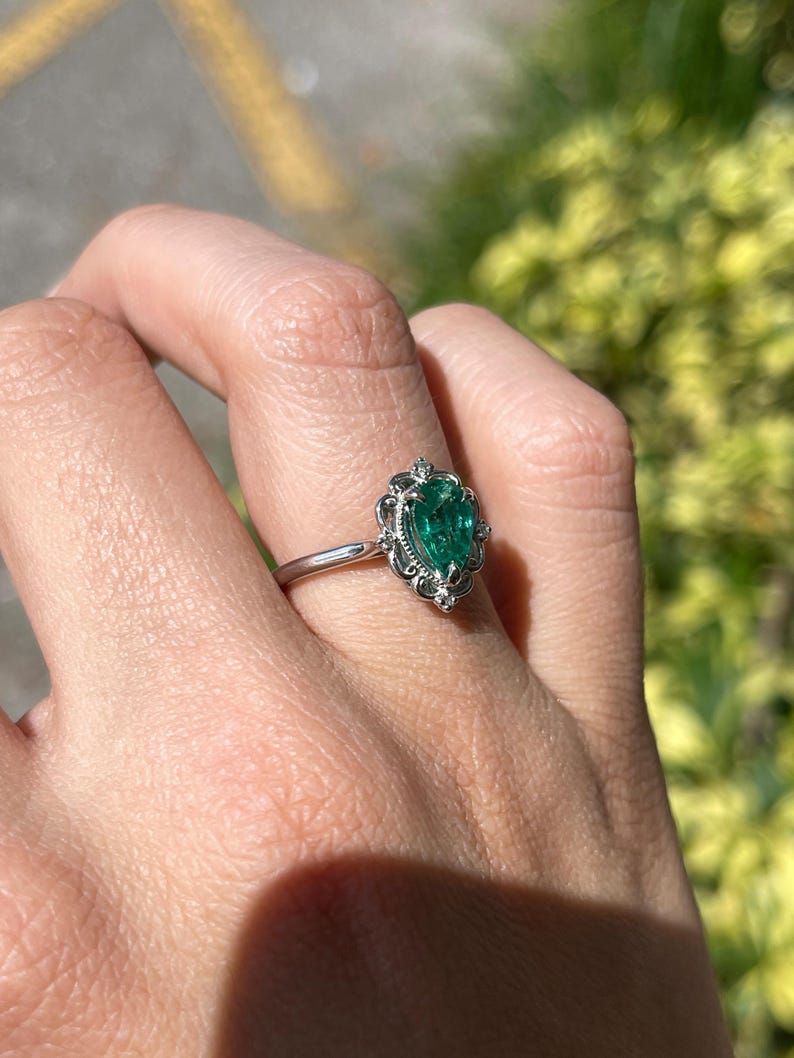 Platinum engagement ring with pear-cut emerald and diamond accents, featuring filigree crown scroll design by Colombian Emerald.