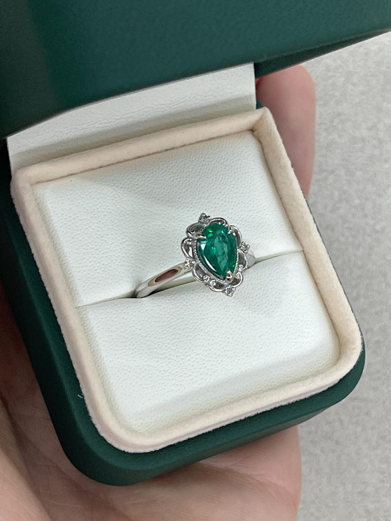 Platinum engagement ring with pear-shaped emerald center, diamond accents, and intricate filigree scroll design by Colombian Emerald