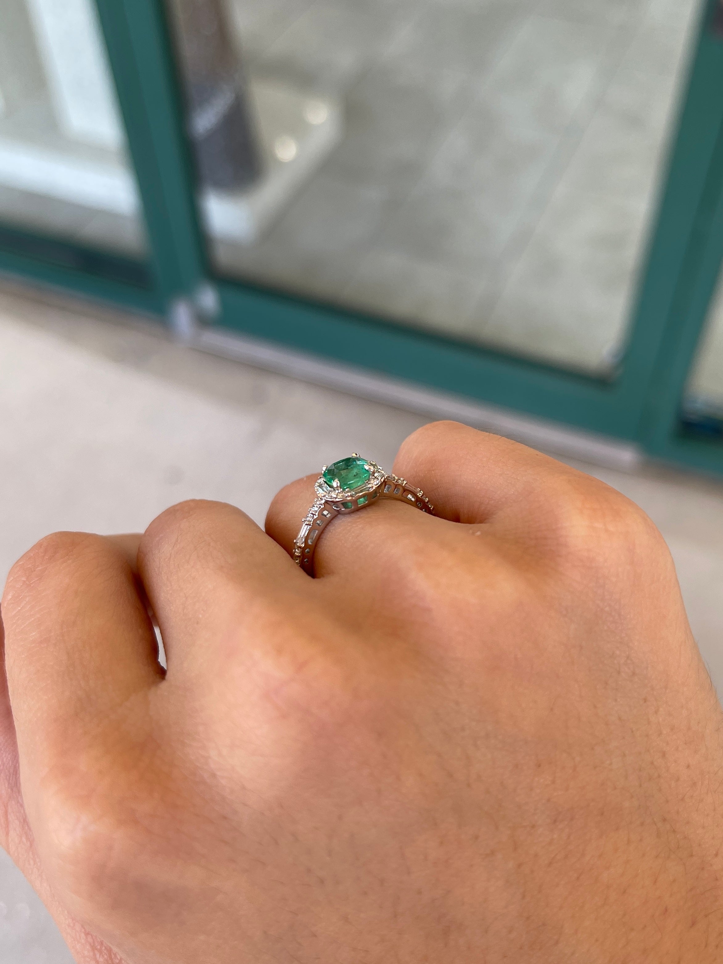 Vivid medium green cushion cut emerald with diamond halo engagement ring featuring round baguette diamonds in 14K gold.
