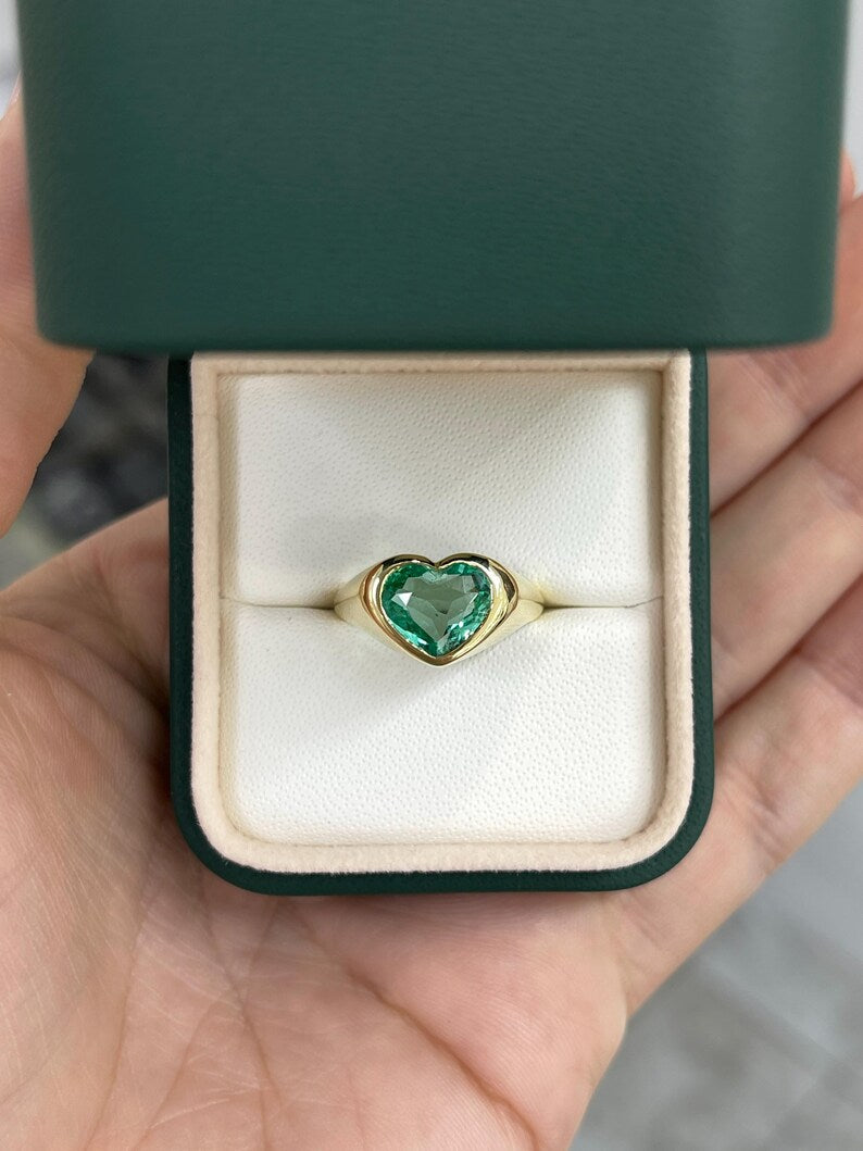 Unisex engagement ring featuring an 18K gold bezel-set heart-cut Colombian emerald, with a remaining balance label.