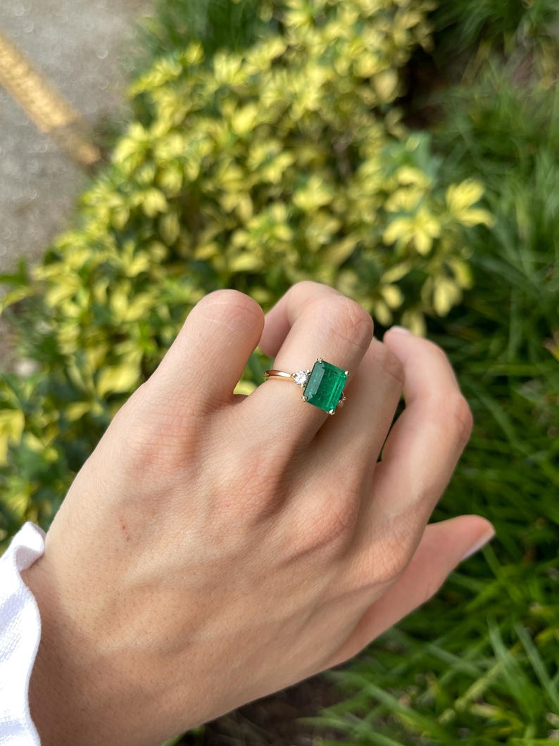 Colombian Emerald 14K gold engagement ring with green emerald cut and round diamonds, three-stone design, elegant and sparkling.