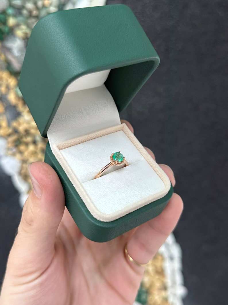 14K rose gold engagement ring with 0.90ct round cut emerald solitaire on a right hand, featuring a sleek, elegant design.