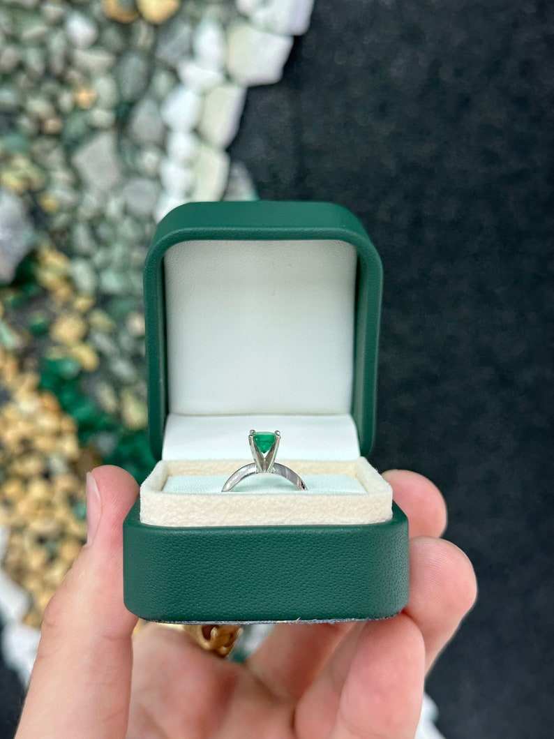 14K white gold engagement ring with a 0.93ct medium dark green emerald round-cut solitaire and four prongs.