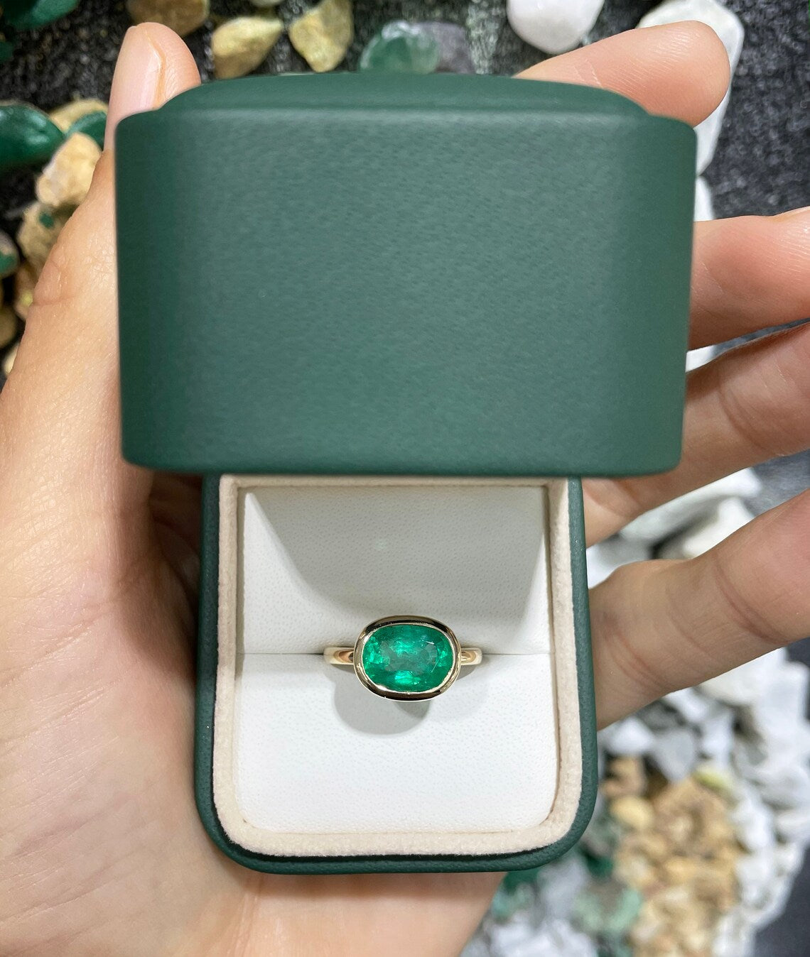14K gold oval emerald solitaire ring with east-west bezel setting, featuring a rich green Colombian emerald gemstone.