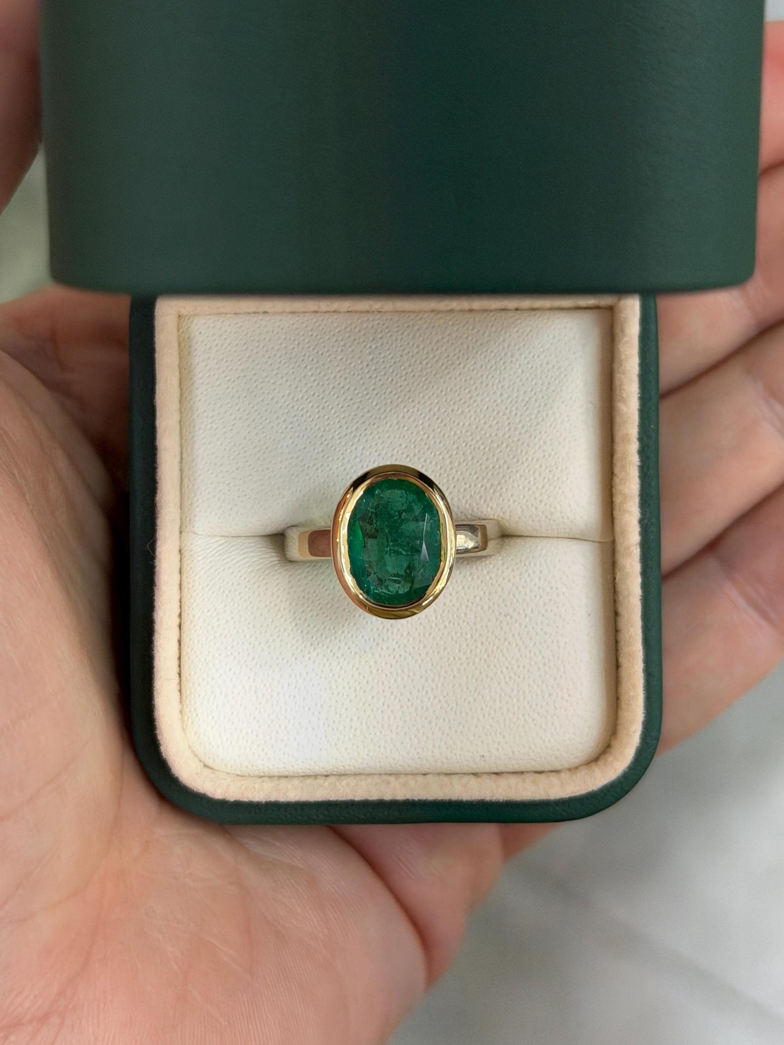 close up view of 3.85ct oval emerald with rich green gemstone two‑toned gold