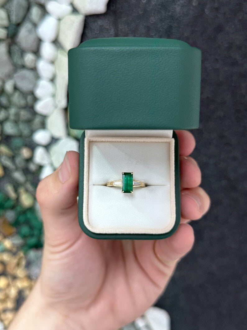 14K gold three-stone engagement ring with dark green emerald and tapered baguette diamond accents, showcasing elegant gemstone details.