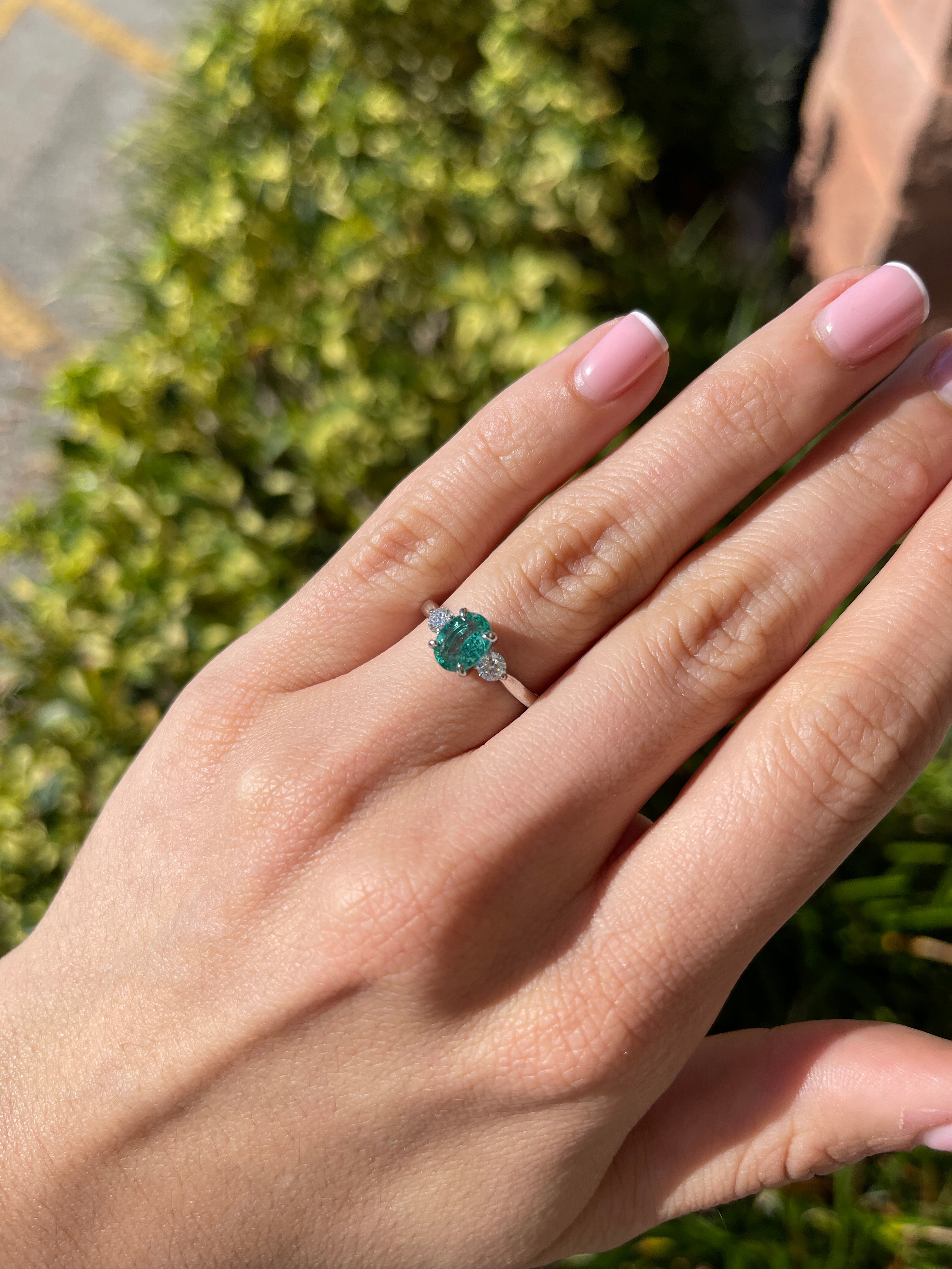14K gold three-stone ring with an oval cut bluish-green emerald and round lab diamonds, featuring a sophisticated design.