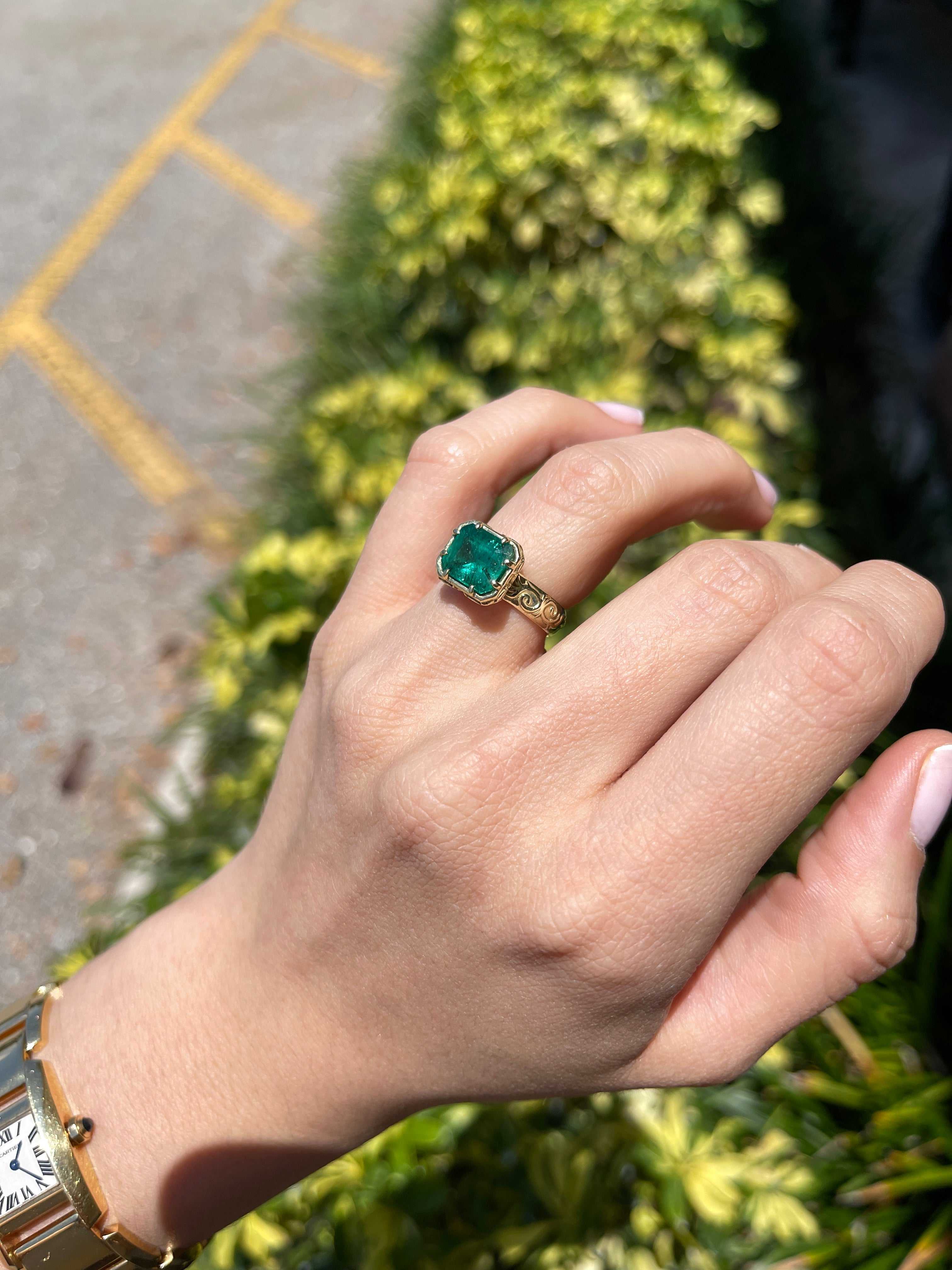 14K gold solitaire emerald ring with 3.65ct east-to-west freckled earth-mined emerald and intricate scroll gold detailing.