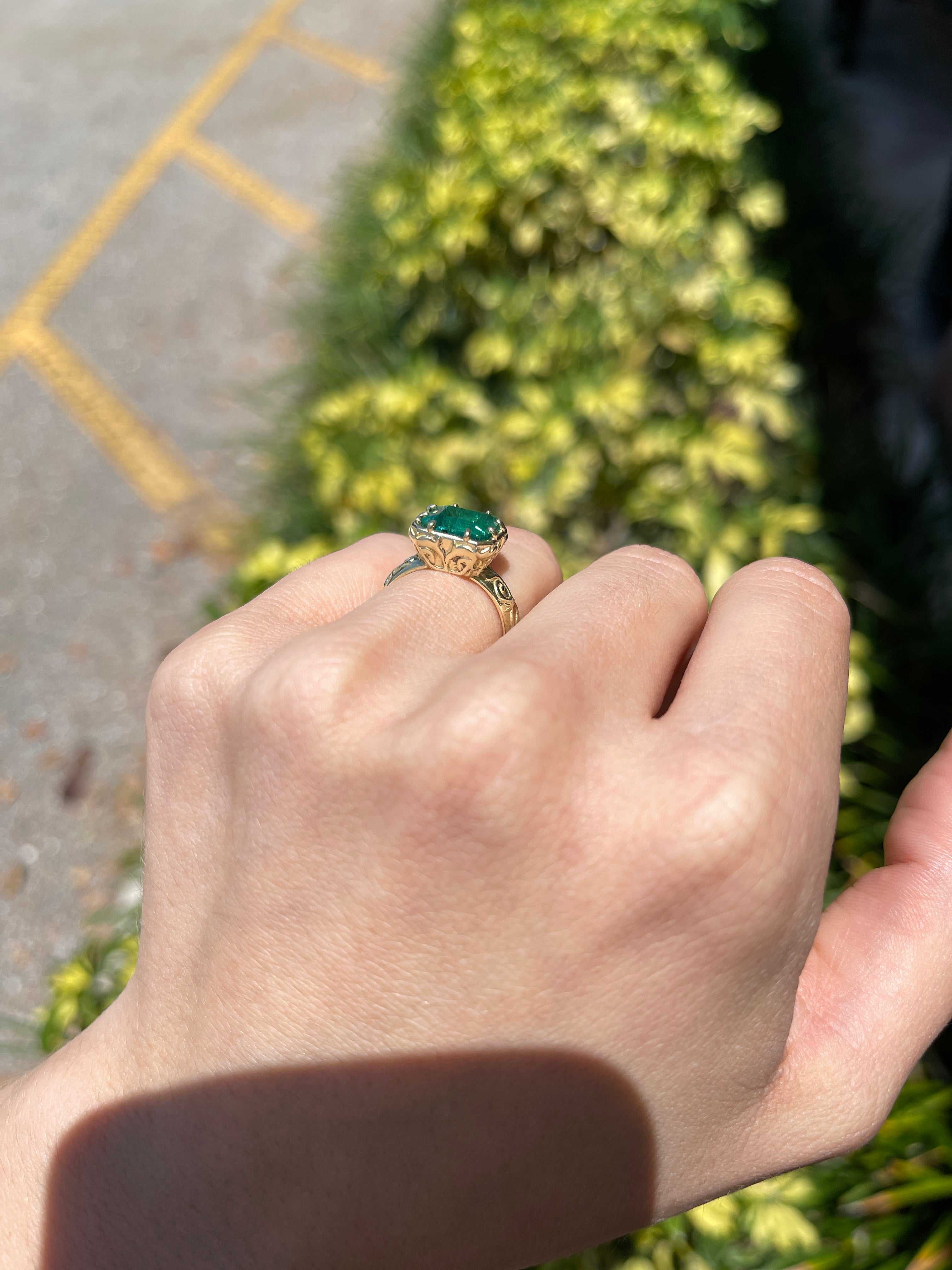 14K gold solitaire emerald ring featuring a 3.65ct east-to-west freckled earth-mined emerald with scroll and etched gold detailing.
