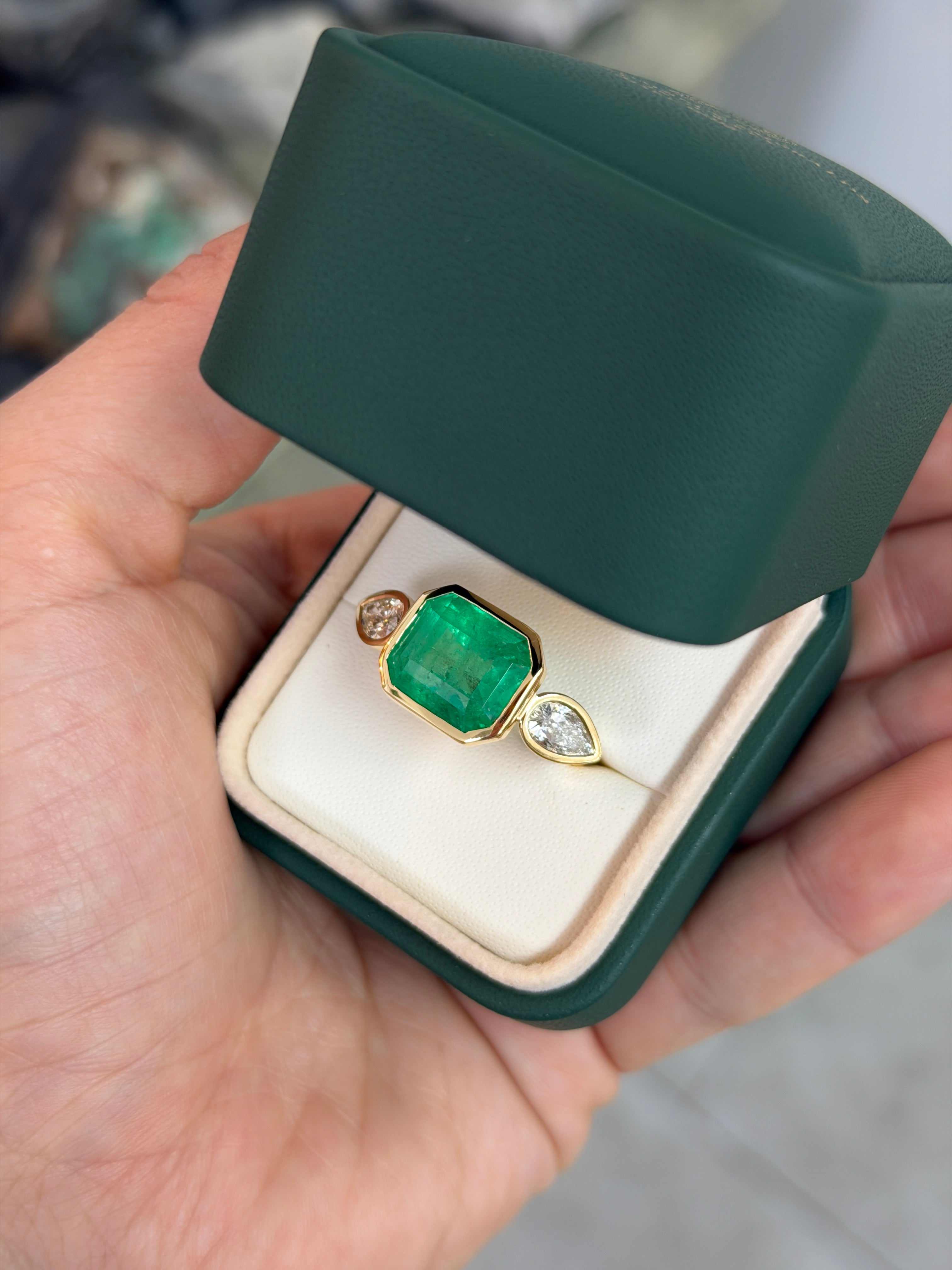 East to West Colombian emerald and pear diamond three-stone ring in 18K gold, featuring vibrant green emeralds and sparkling diamonds.