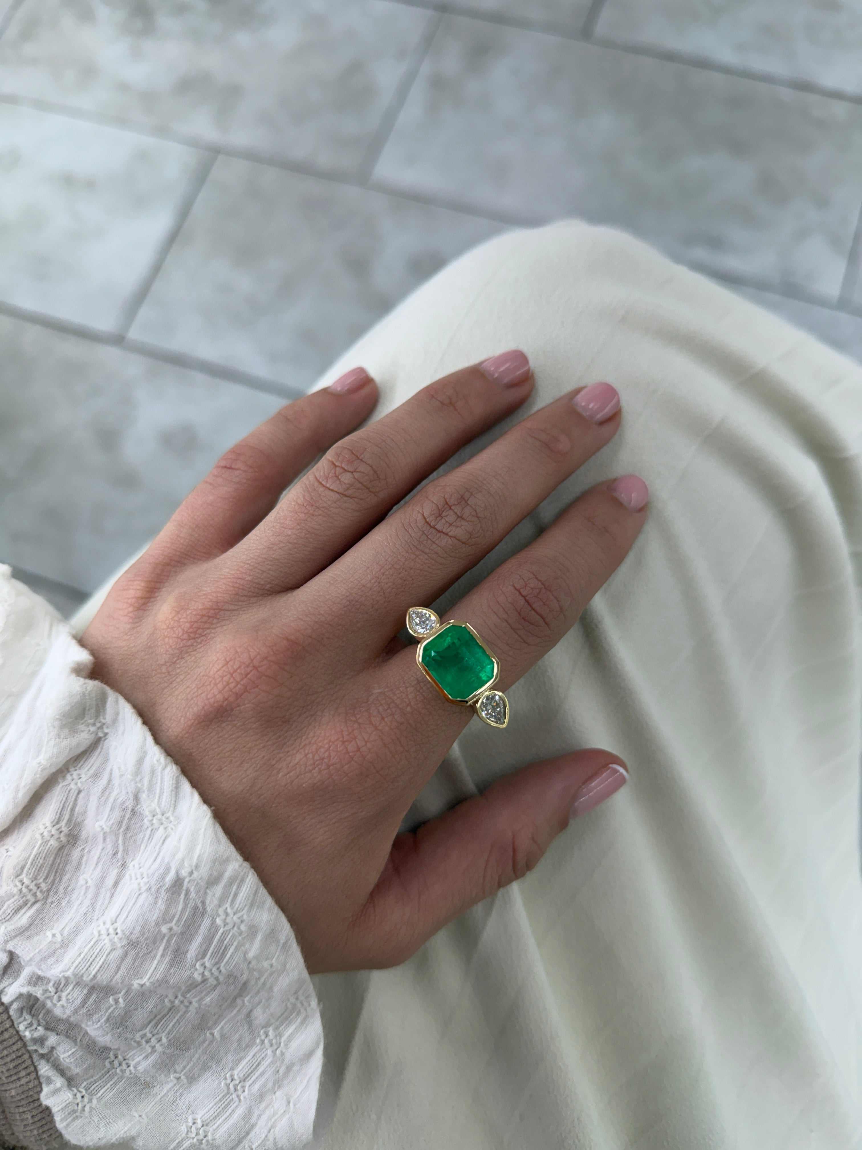 East to West Colombian emerald and pear diamond three-stone ring in 18K gold by JR Colombian Emeralds, showcasing vibrant gemstones.