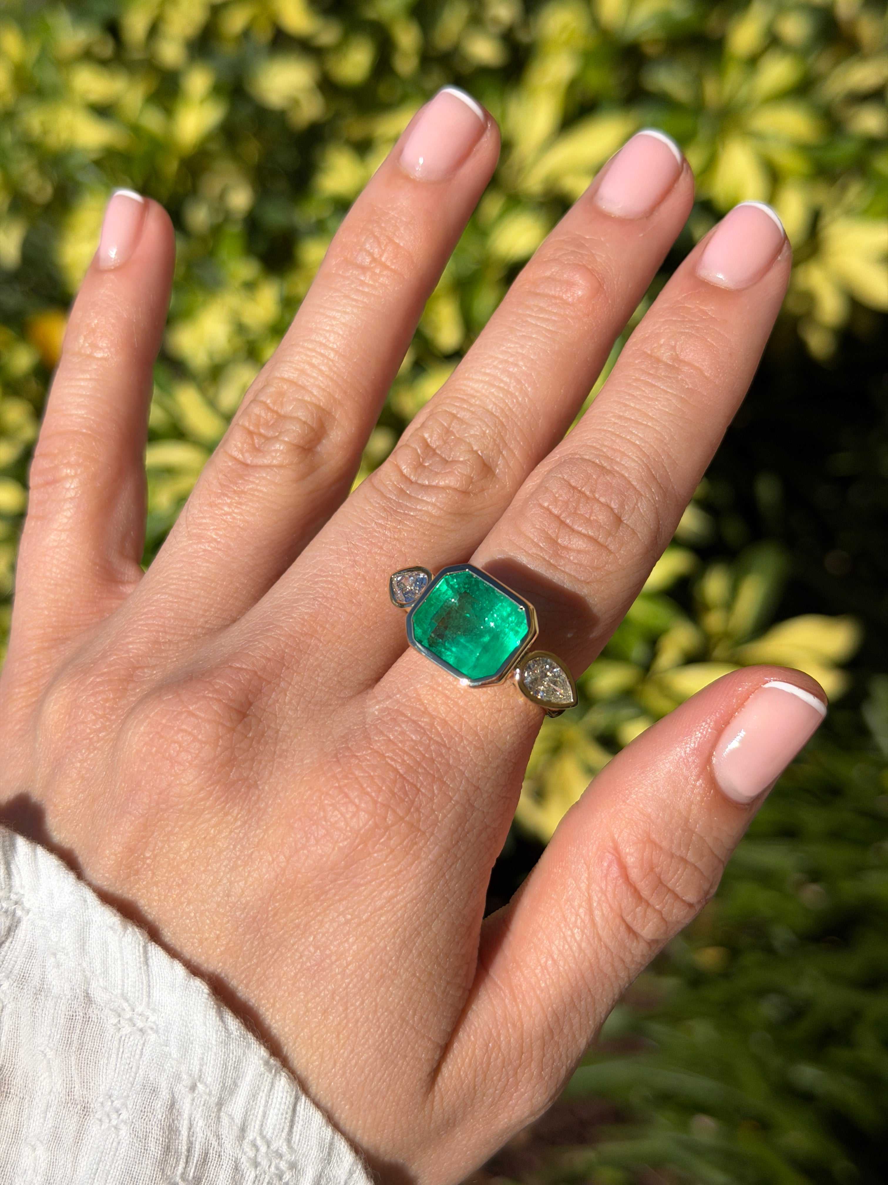 East to West Colombian emerald and pear diamond three-stone ring in 18K gold, featuring vibrant green emeralds and sparkling diamonds.