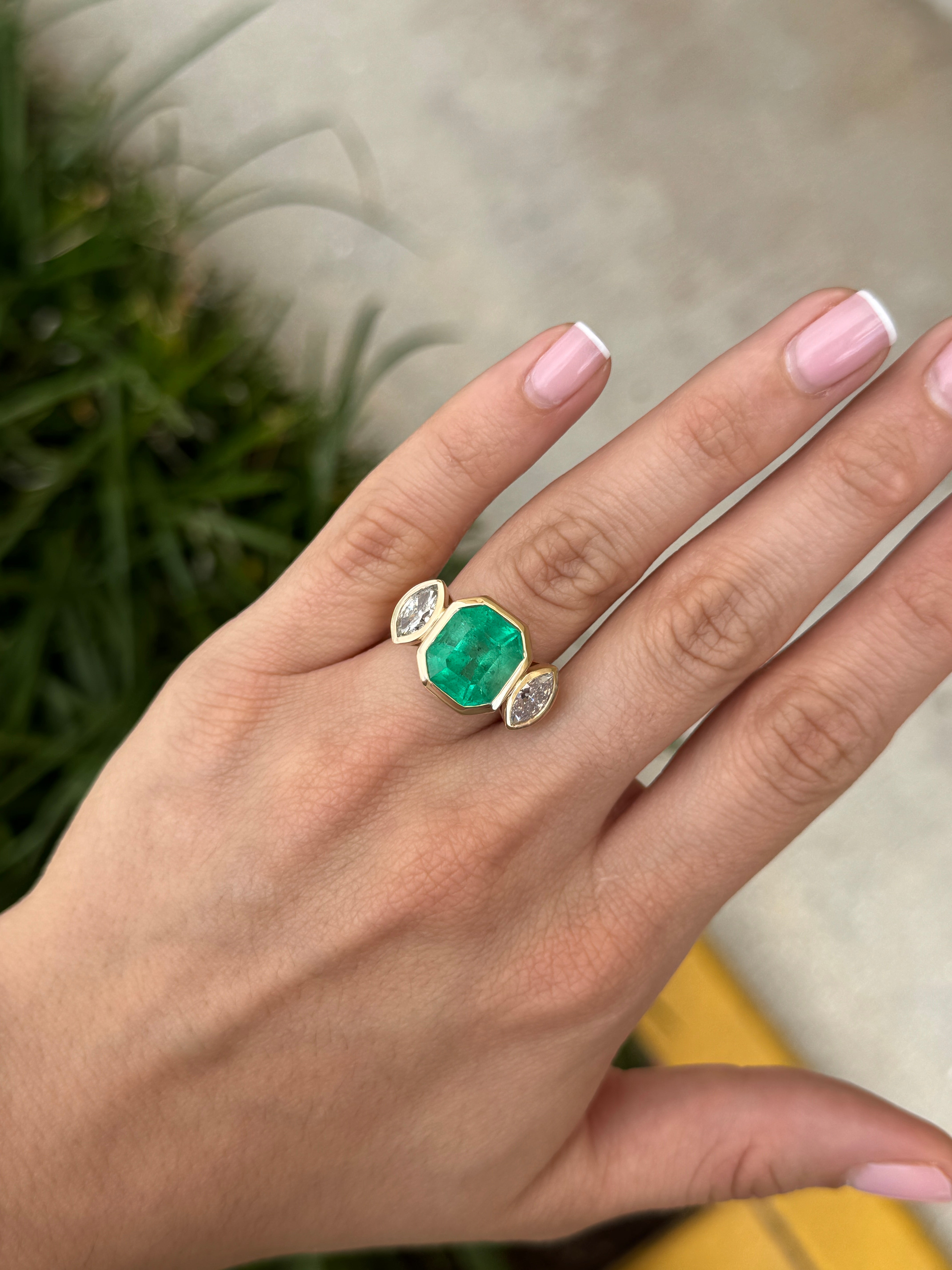 Emerald cut Colombian emerald and marquise diamond trilogy ring in 18K gold, showcasing vibrant gemstones and intricate bezel setting.