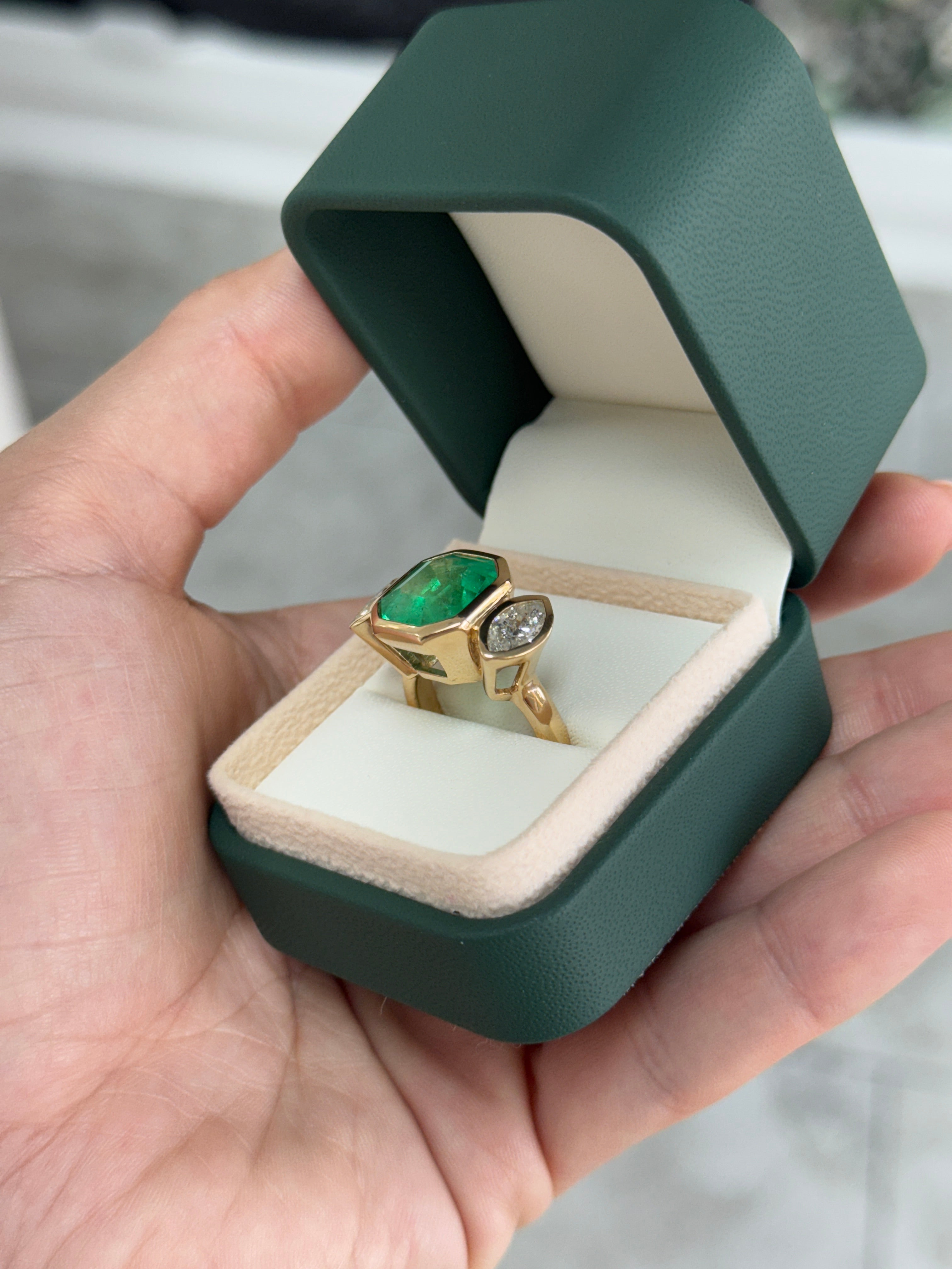 Emerald cut Colombian emerald and marquise diamond trilogy ring in 18K gold featuring bezel setting and detailed craftsmanship.