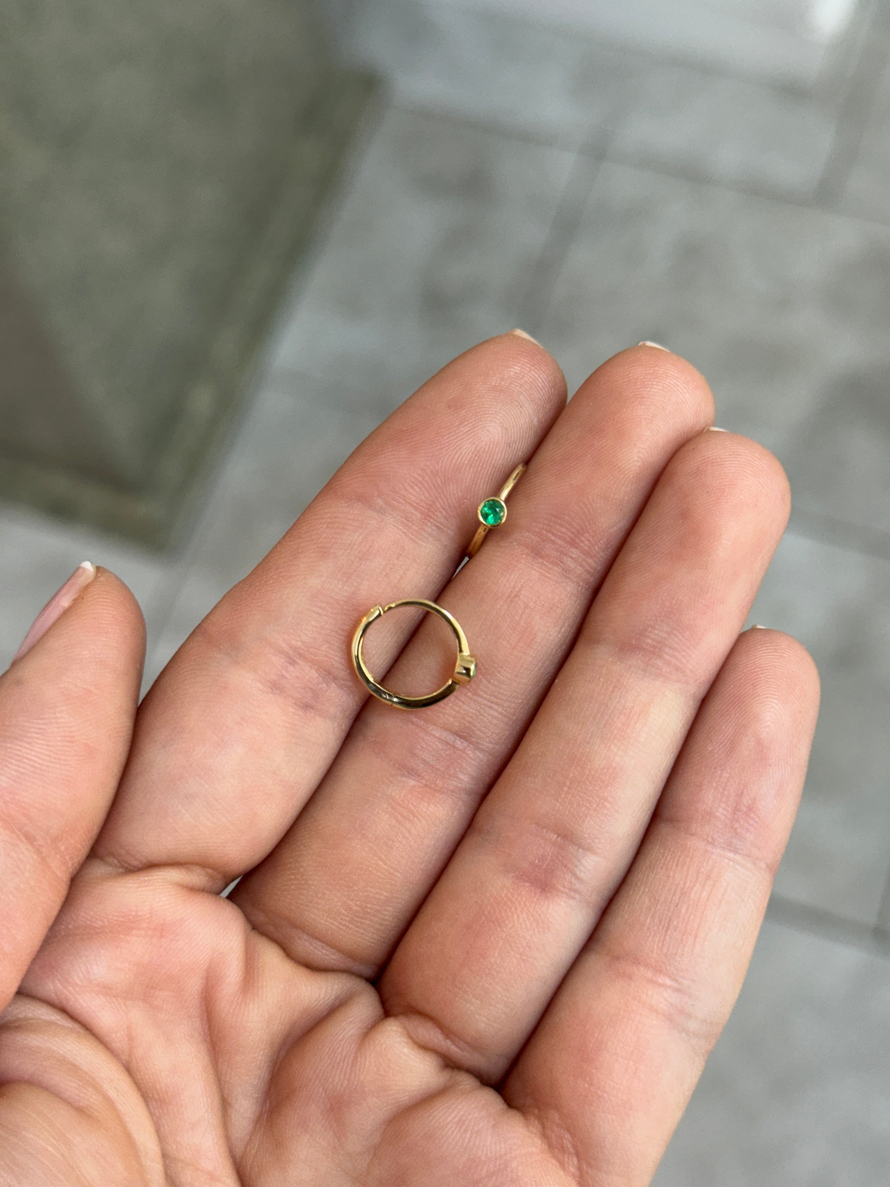 14K gold emerald huggie earrings with 0.13tcw bezel-set Colombian emeralds, shown in a close-up image.