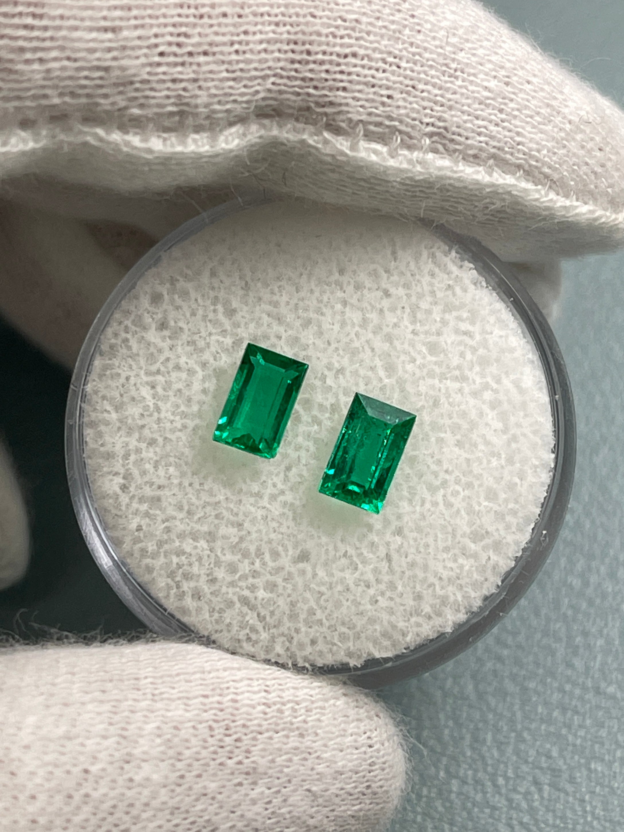 Matching pair of 0.99tcw green natural Colombian emerald baguette cuts by JR Colombian Emeralds on a white background.