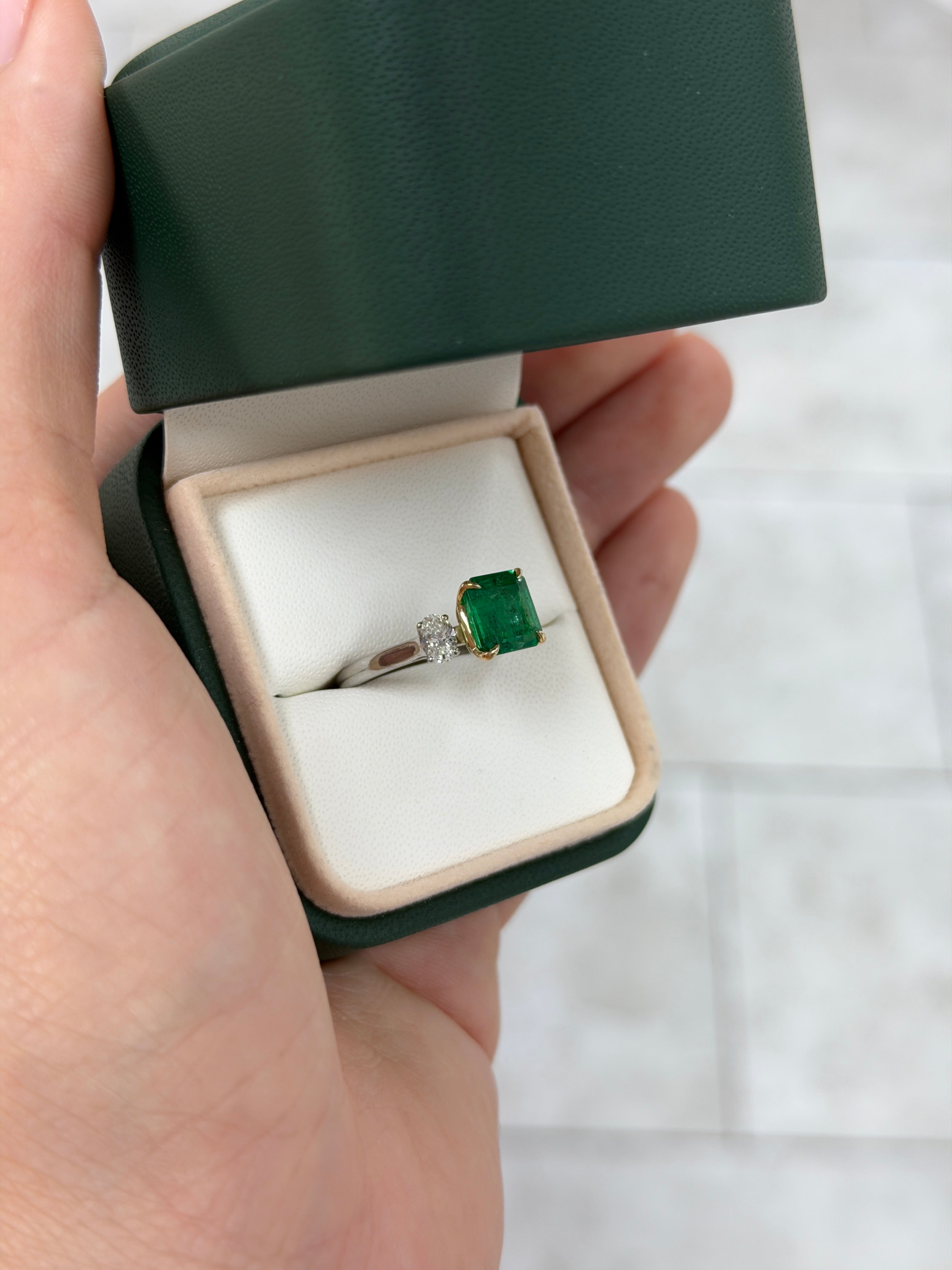 18K gold three-stone ring with vivid asscher cut emerald and oval diamonds, featuring platinum accents by JR Colombian Emeralds.