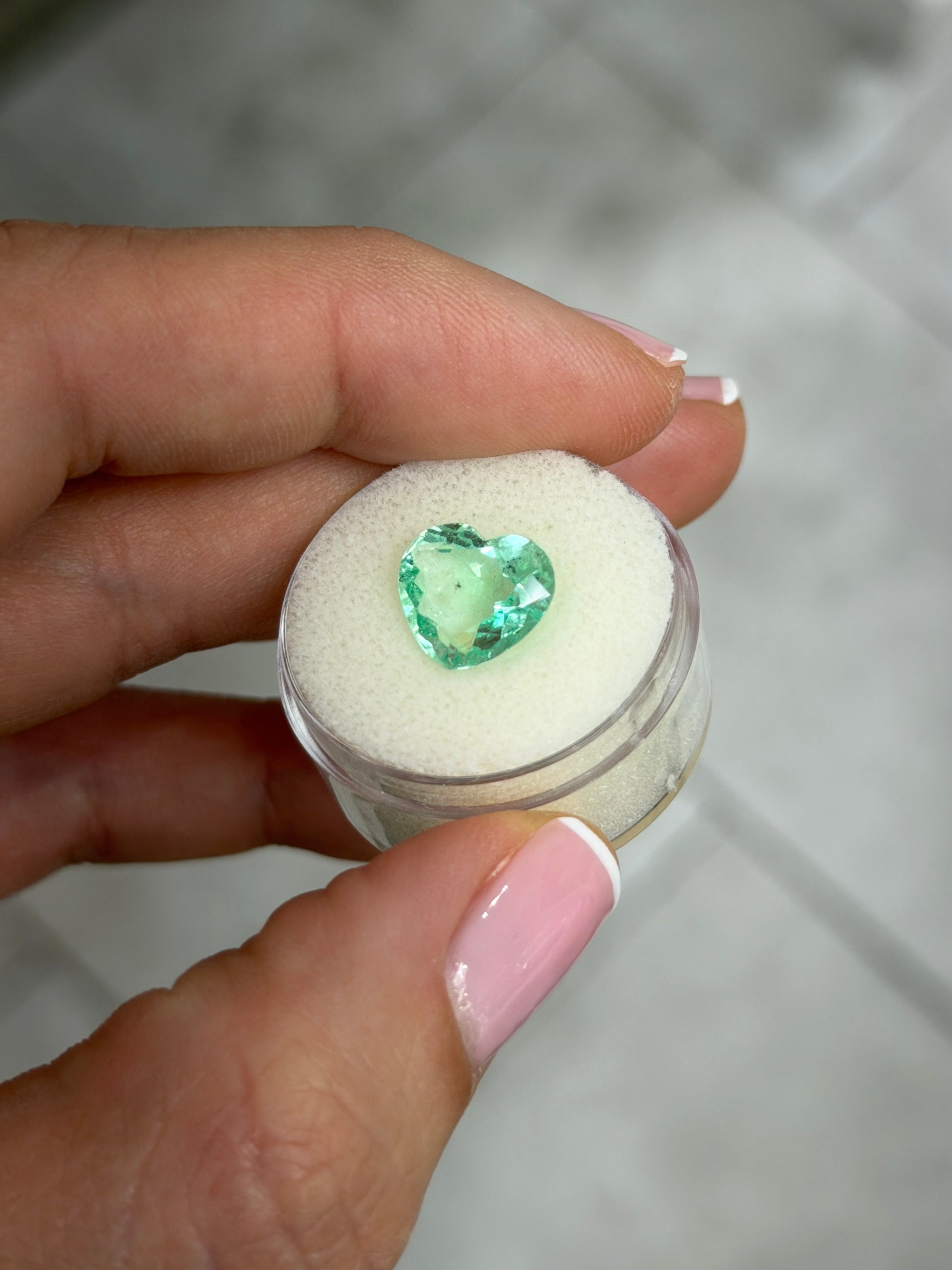 Light bluish green 3.44 carat Colombian emerald in 10x11 portrait cut with natural freckles, heart-shaped loose gemstone.
