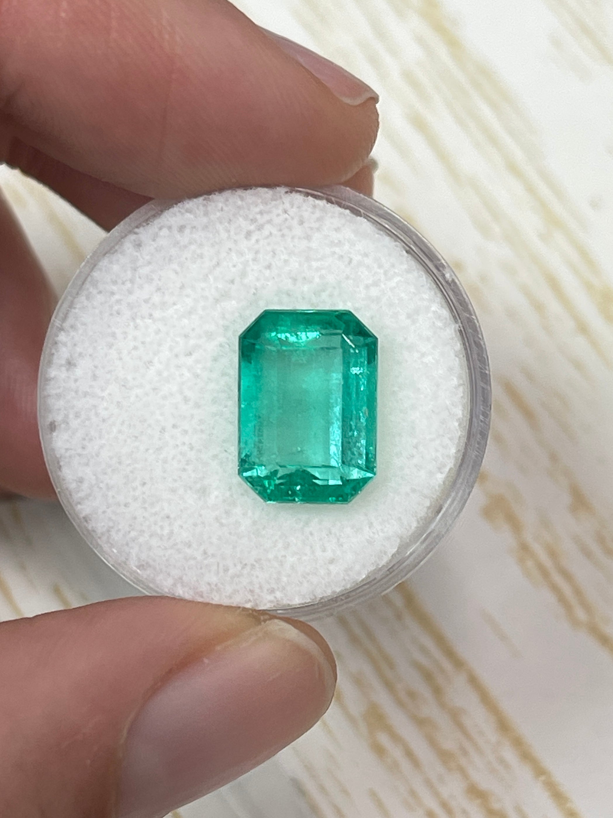Loose 5.54 carat spring green Colombian emerald in elongated emerald cut, natural and vibrant, displayed by JR Colombian Emeralds.